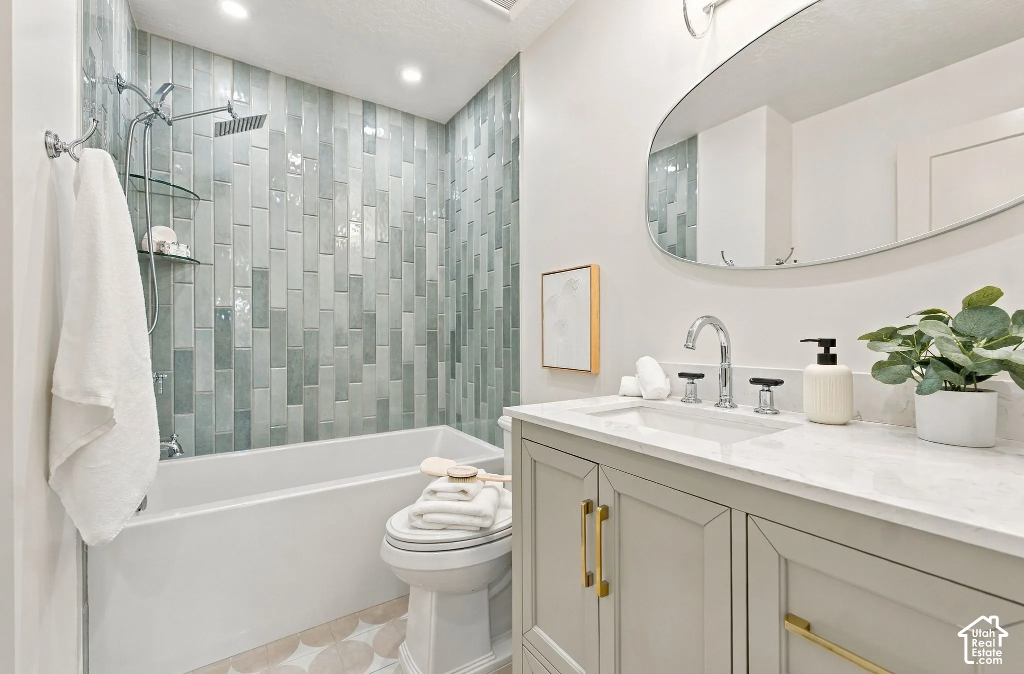Spa-inspired bathroom featuring a subway tile shower surround with geometric pattern detailing, freestanding soaking tub, white quartz countertop with dual-sink vanity, brass hardware accents, and an arched mirror with integrated lighting