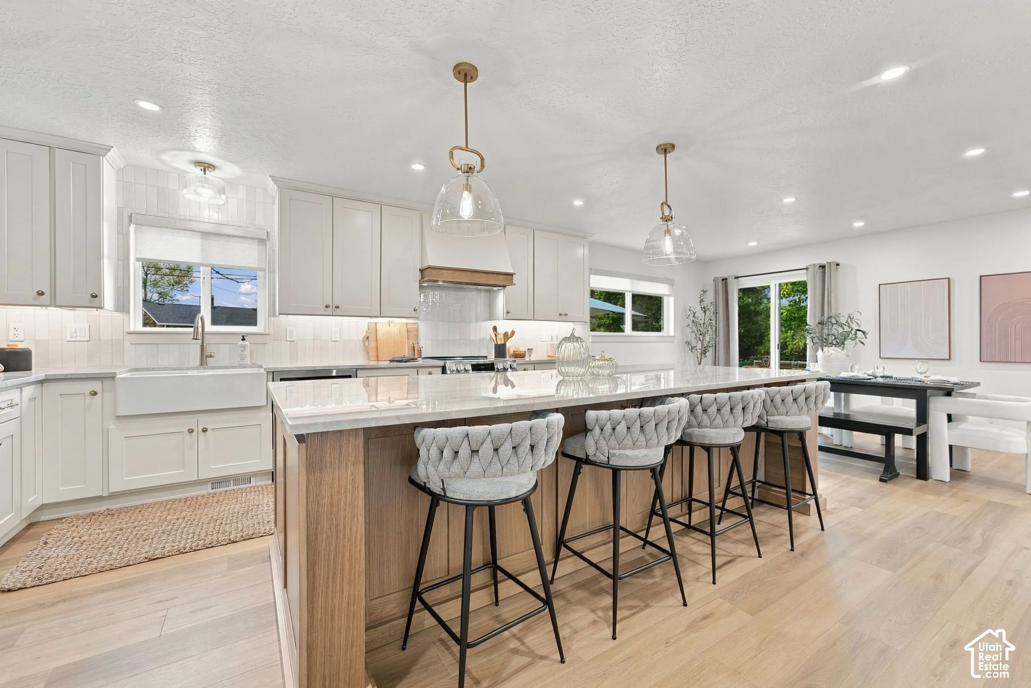 Kitchen featuring white shaker-style cabinetry, an expansive center island with wood-tone base, apron-front sink, stone-finish countertops, and glass pendant lighting