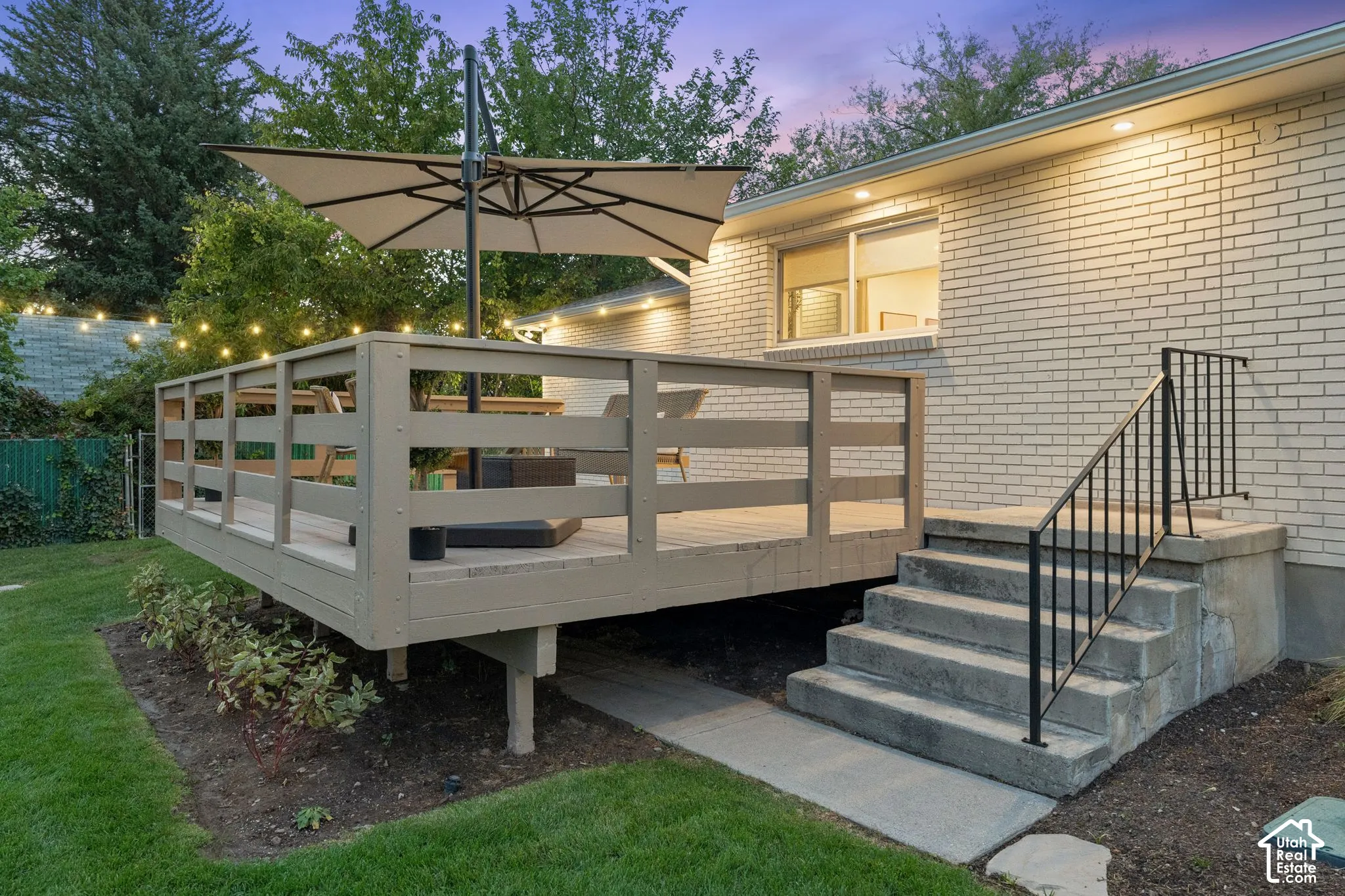 Raised deck with horizontal wood railing, painted brick exterior, and concrete steps featuring a metal handrail