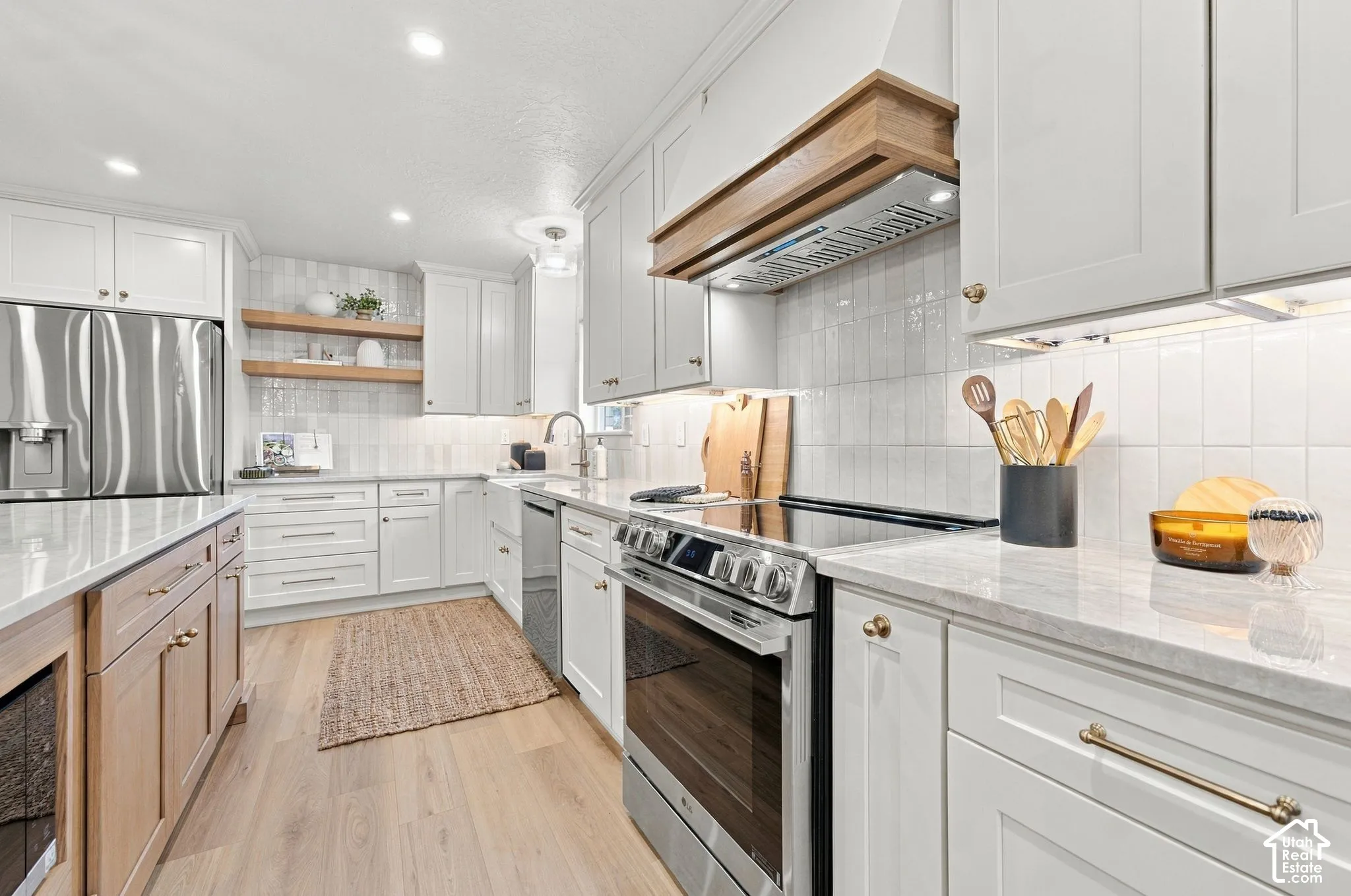 Modern kitchen featuring white cabinetry with brass hardware, stainless steel appliances including a slide-in range, white subway tile backsplash, quartz countertops, and wood-finish flooring throughout the open layout