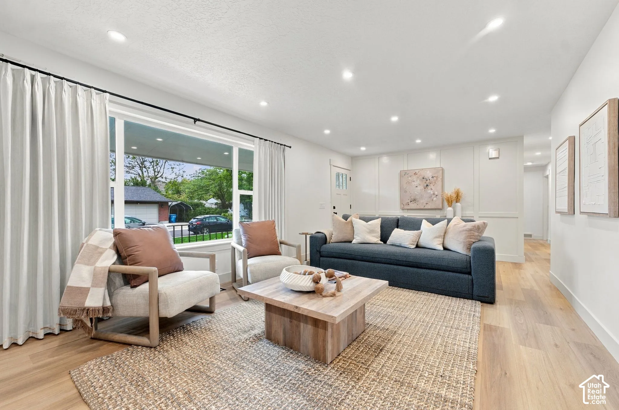 Living area featuring wood-finish flooring, recessed lighting, and expansive picture window with wall-to-wall drapery hardware and wainscoting paneling