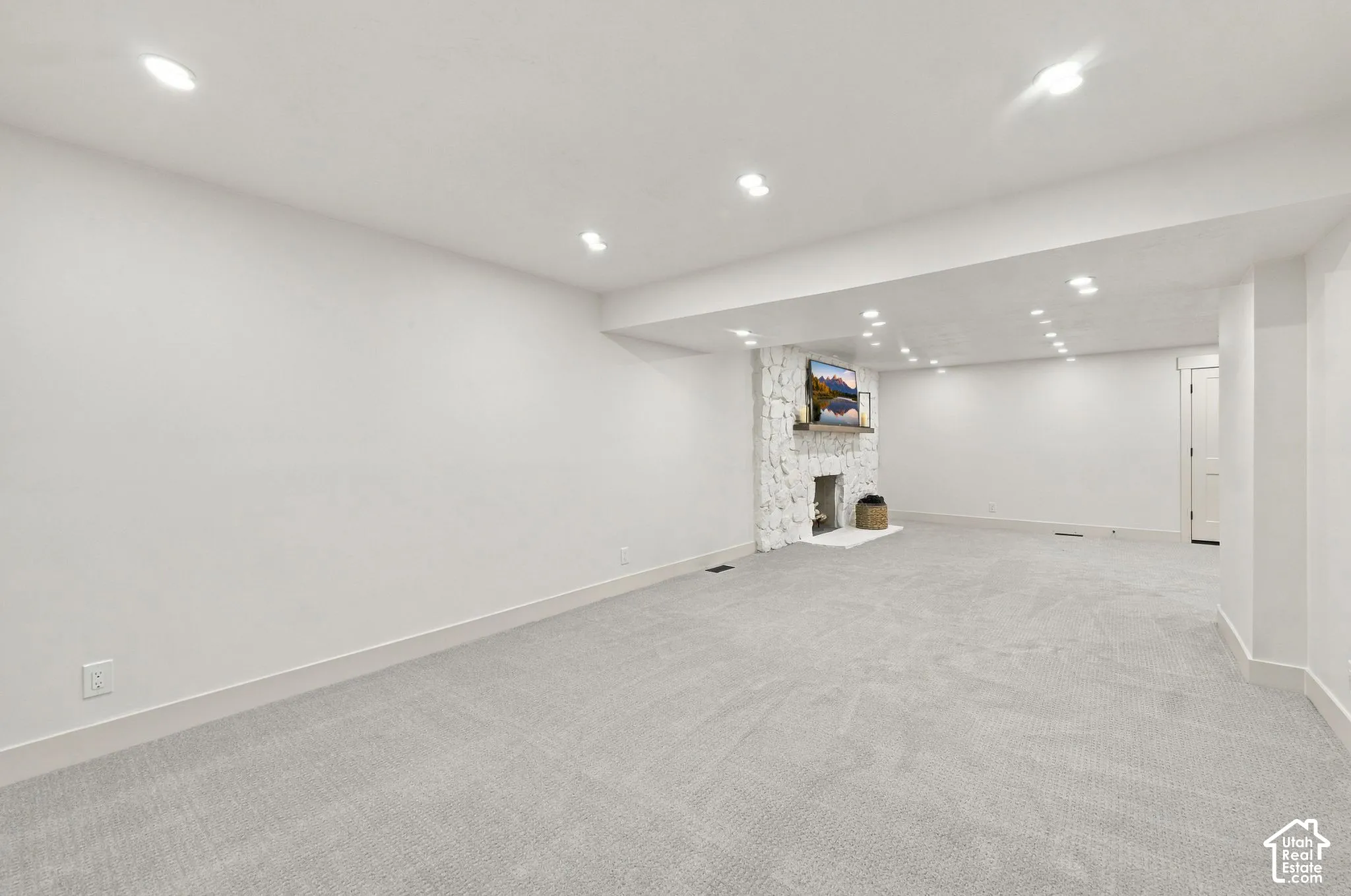 Spacious finished basement featuring neutral carpet flooring, recessed ceiling lighting, and a built-in shelving unit with display space