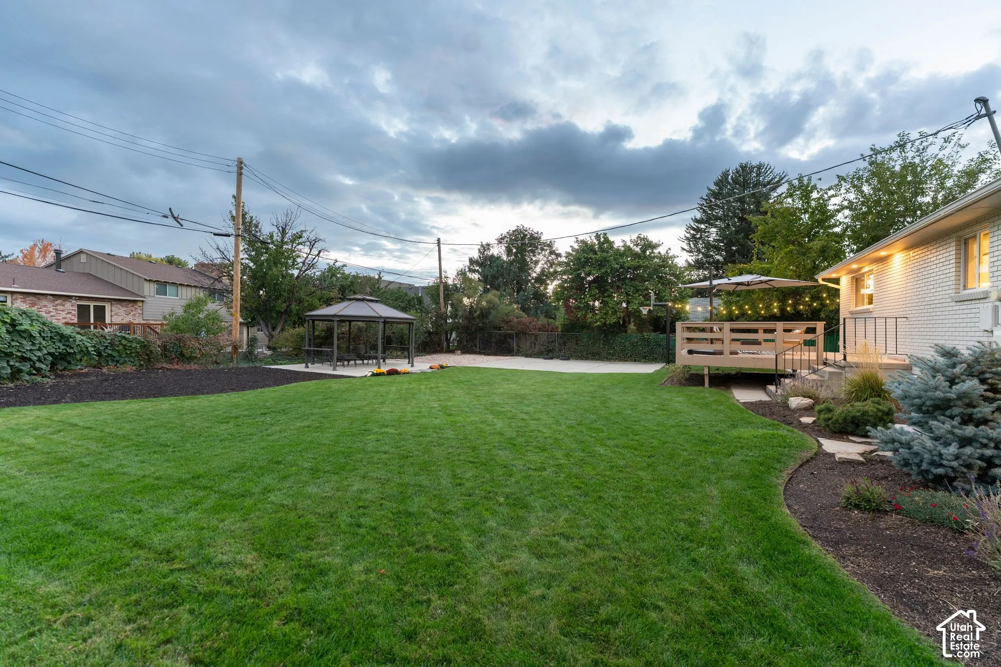 Backyard featuring a manicured lawn, a detached metal-frame gazebo, a raised wood deck with metal railings, and natural landscape beds