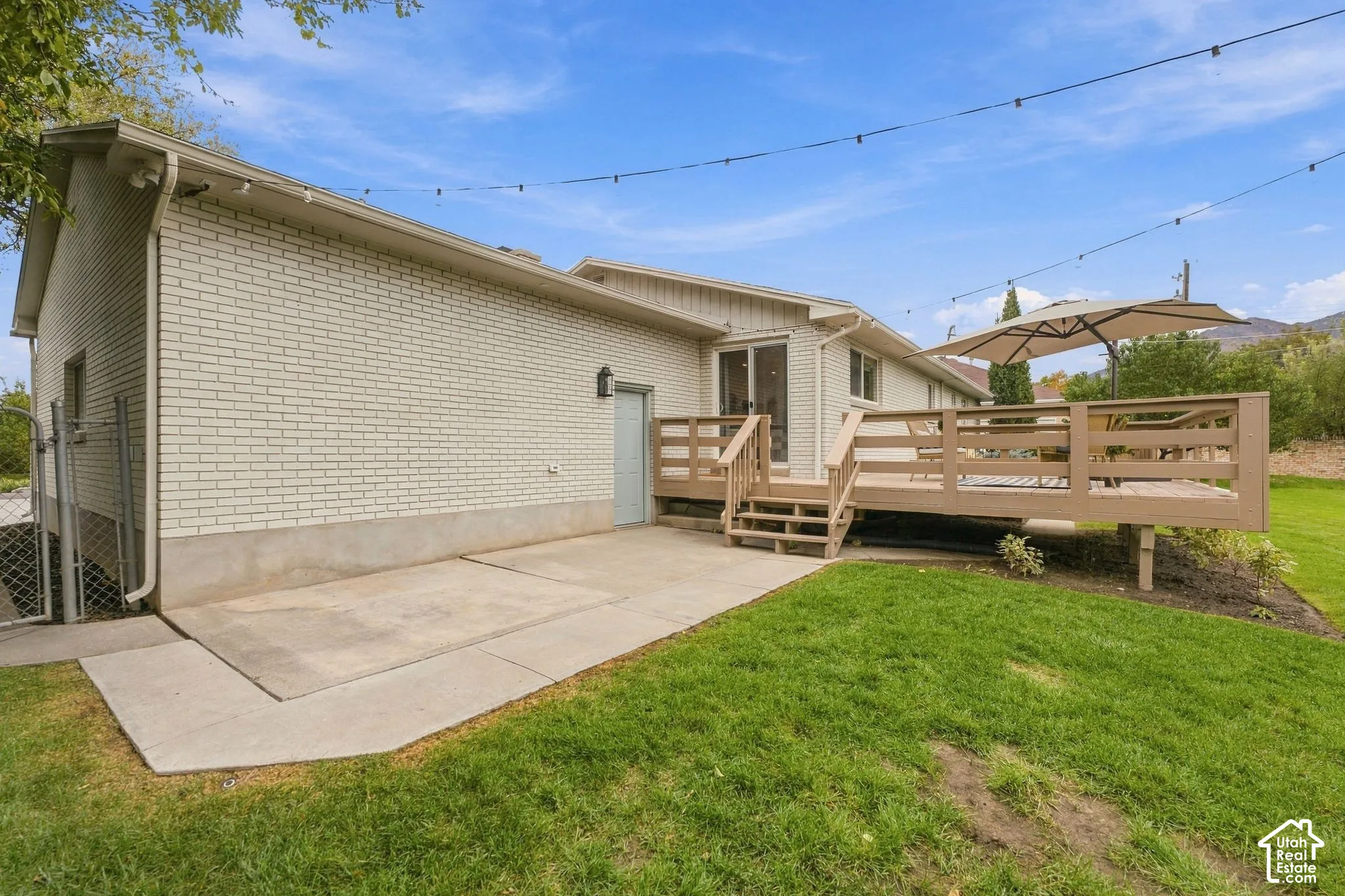 Exterior featuring a painted brick facade, raised wood deck with balustrades, concrete patio, and expansive lawn area