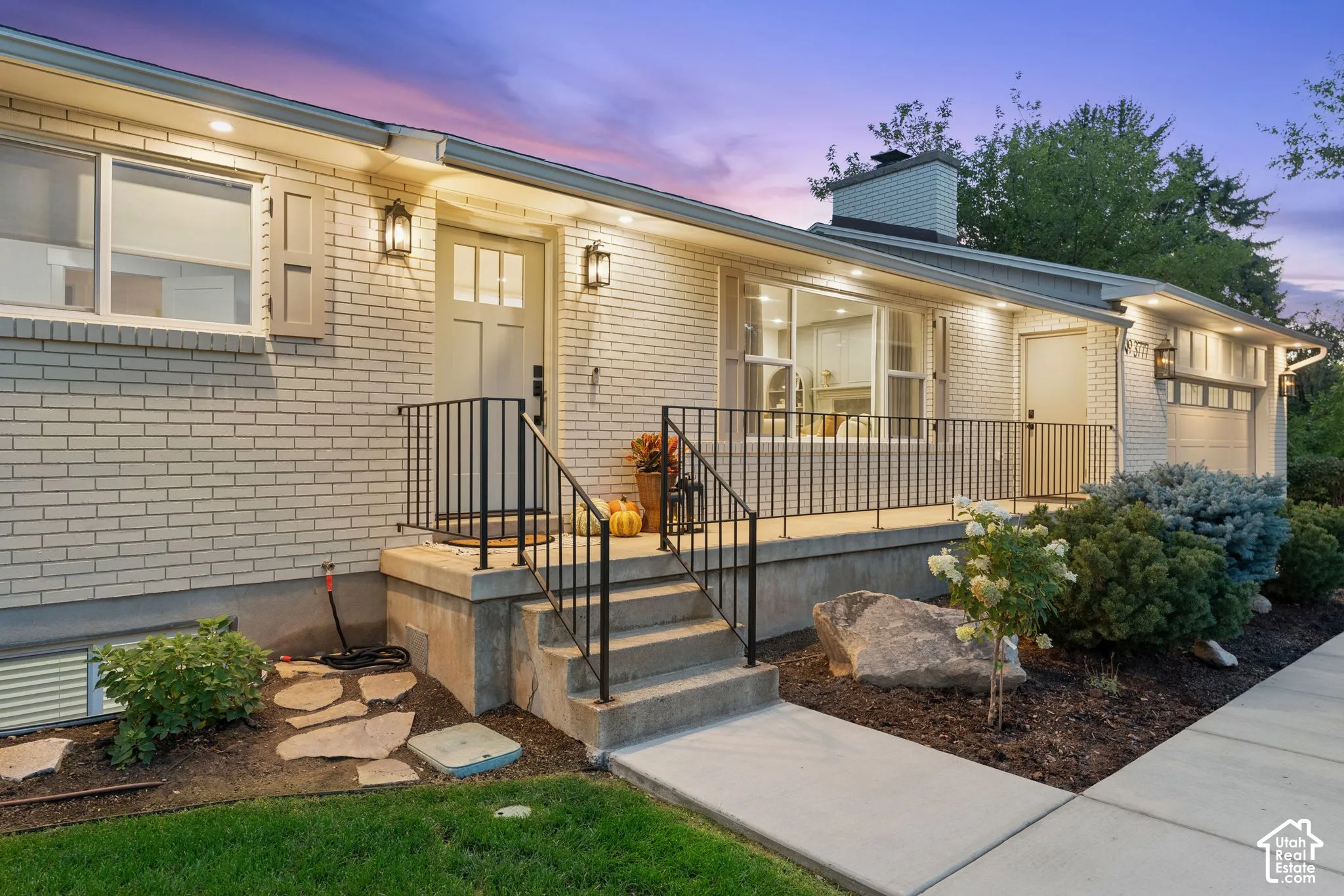 Light-colored brick exterior featuring a covered porch, black metal railings, multi-light front door, and recessed soffit lighting