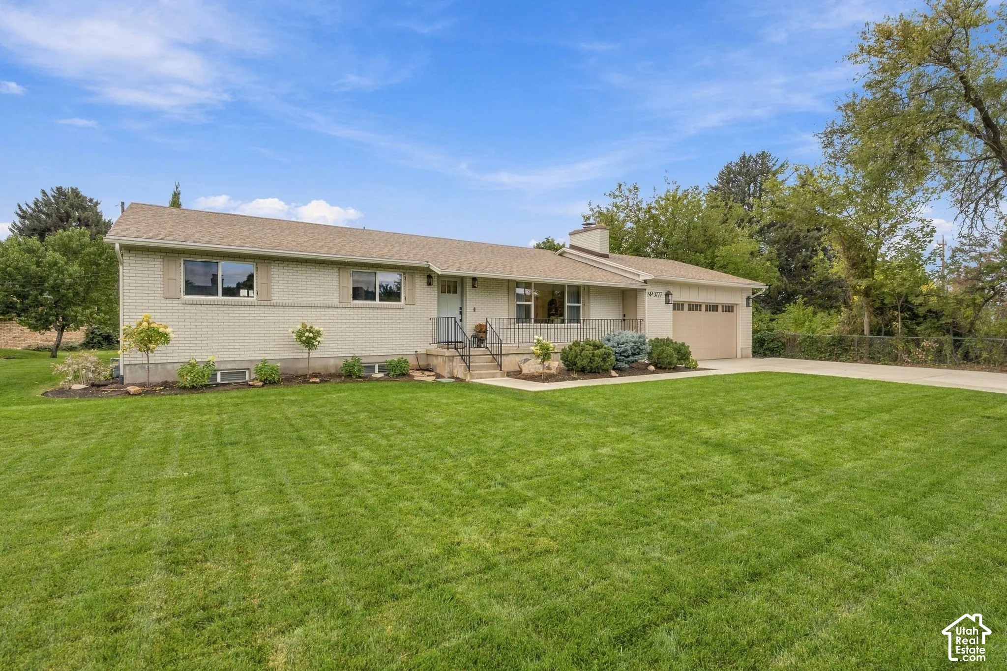 Single-story brick exterior residence featuring a concrete driveway, attached garage, covered entryway with metal railing, and expansive lawn area