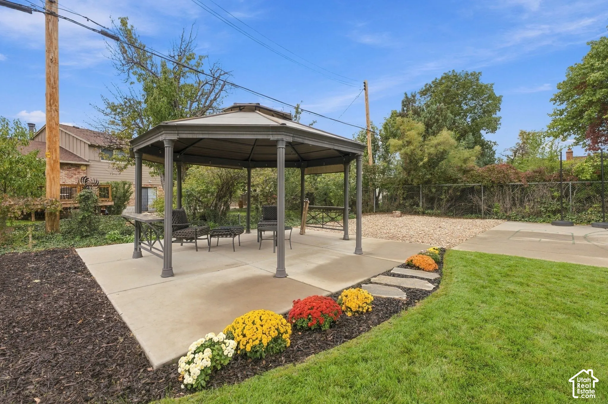 Backyard featuring a permanent metal-framed gazebo, concrete patio, stone garden path, mulched beds, and lawn space