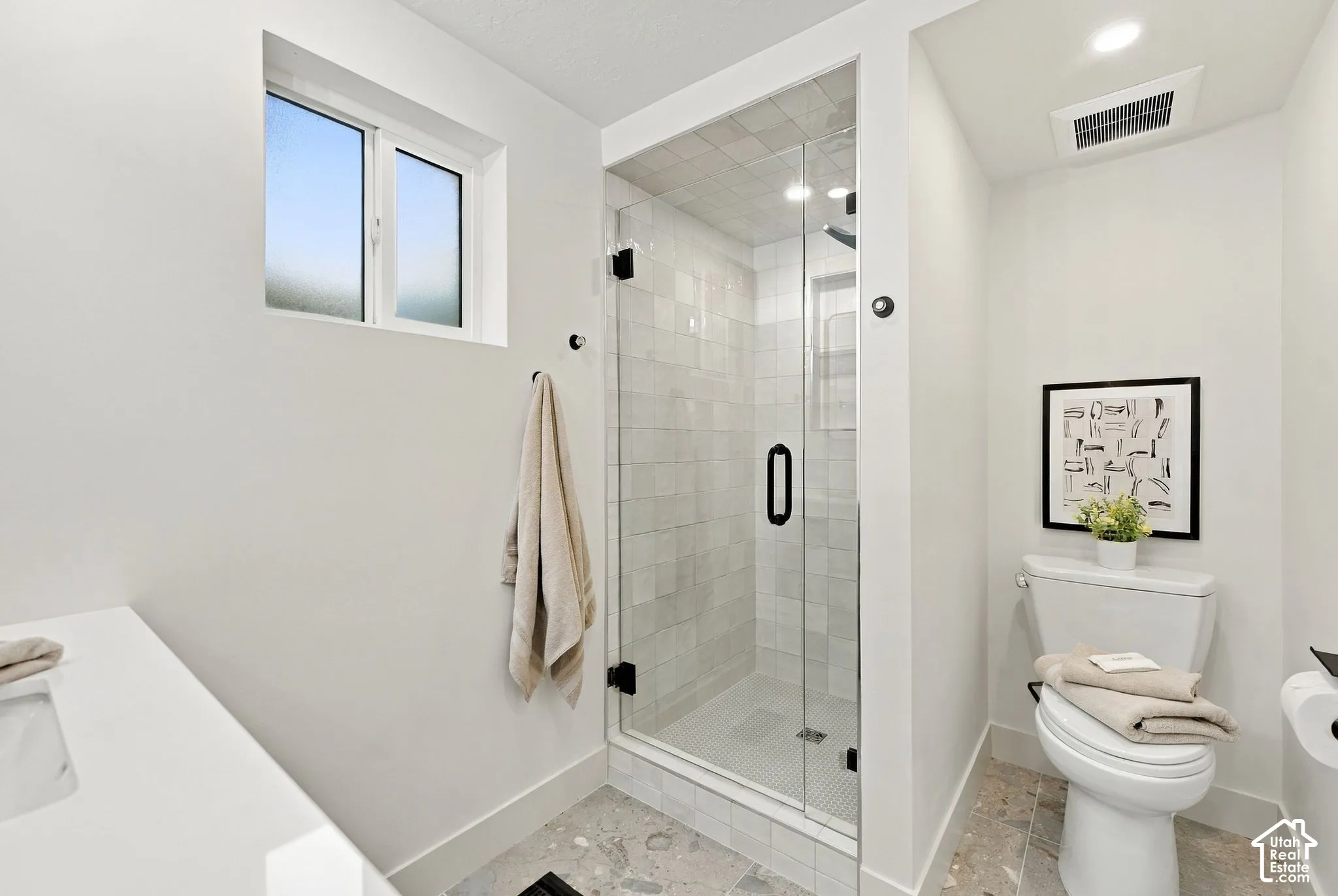 Walk-in shower with a glass door, light-toned subway tile surround, recessed wall niche, and stone-finish floor tile