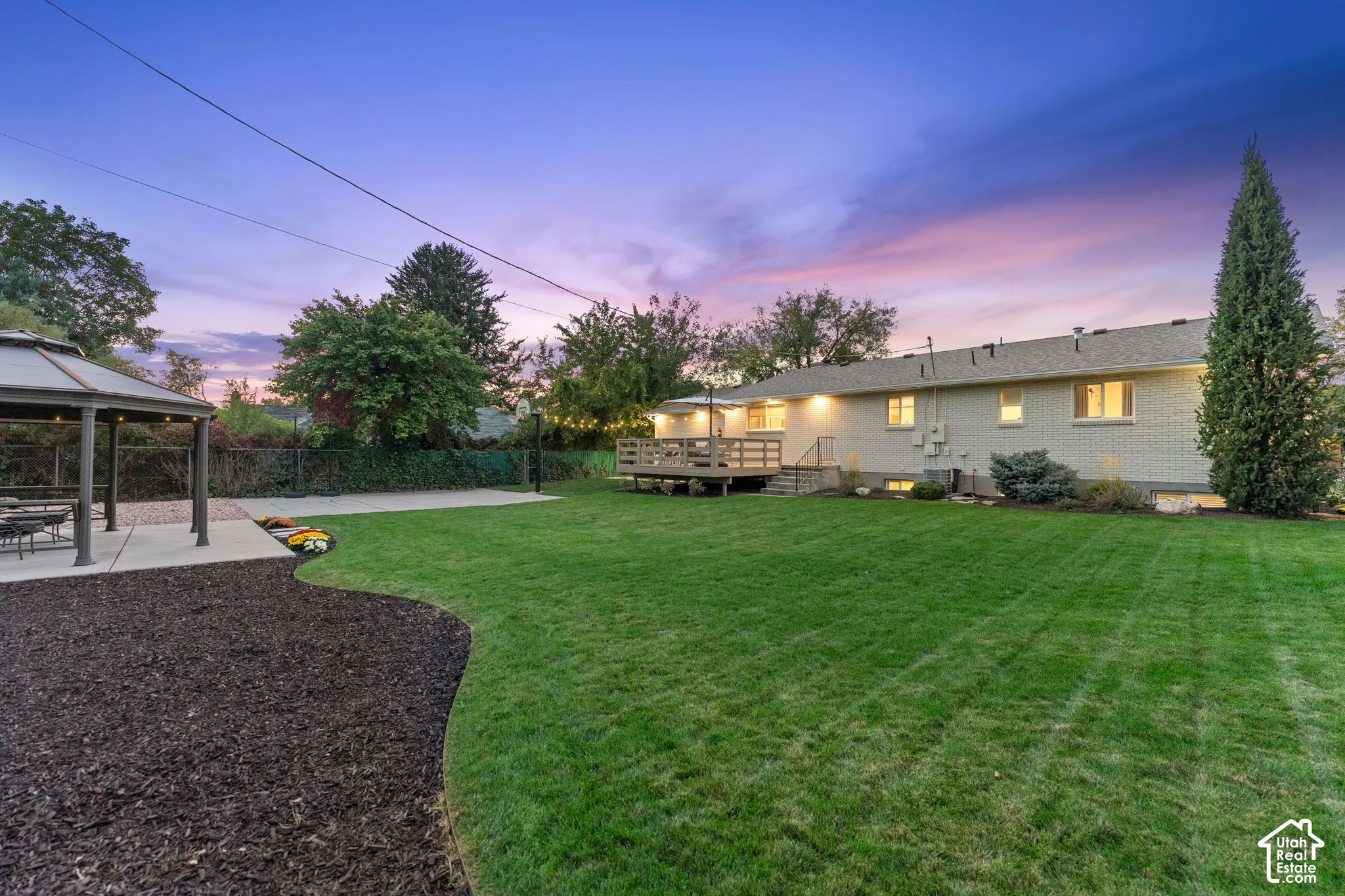 Spacious backyard featuring a manicured lawn, an elevated wood deck, a covered gazebo, and concrete hardscaping