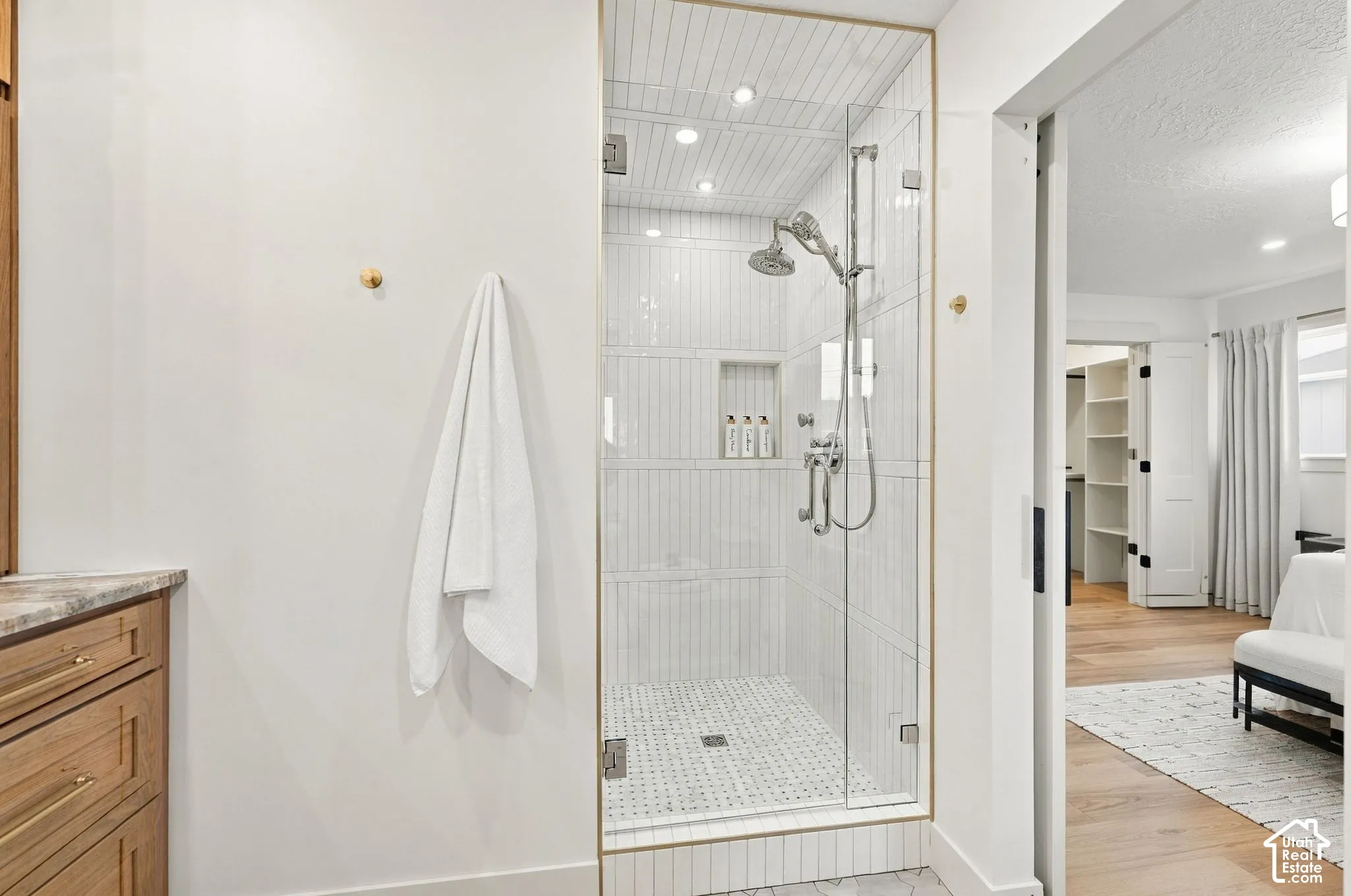 Spa-inspired primary bathroom featuring a frameless glass-enclosed shower with subway tile surround, marble mosaic floor, dual showerheads, and brushed brass hardware