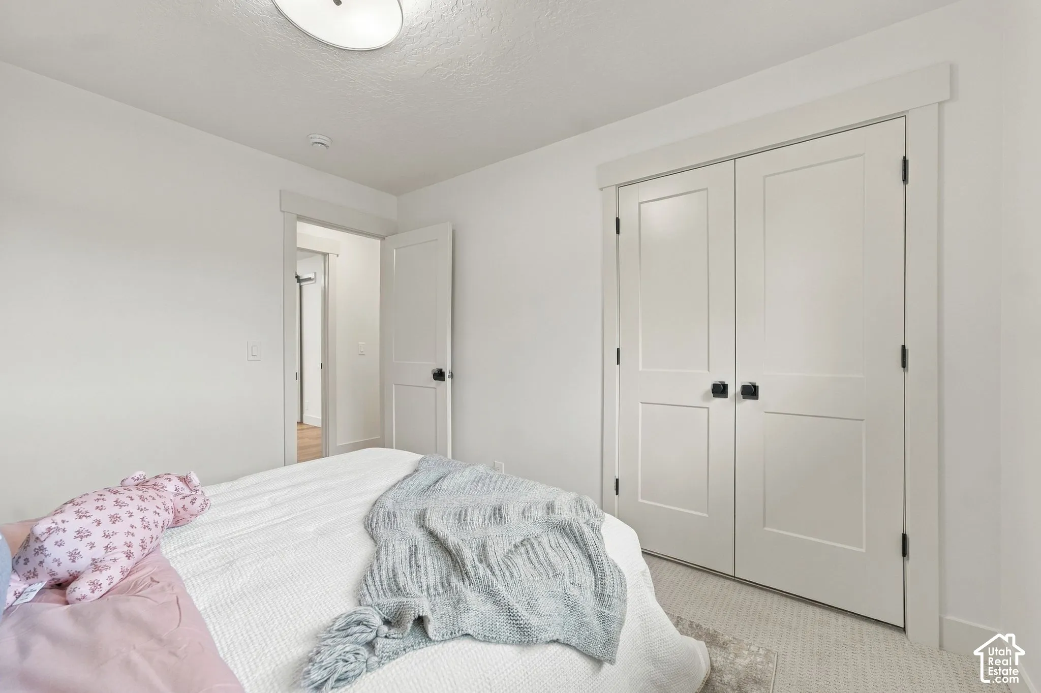Bright secondary bedroom featuring clean white walls, neutral wood-finish flooring, and abundant natural light