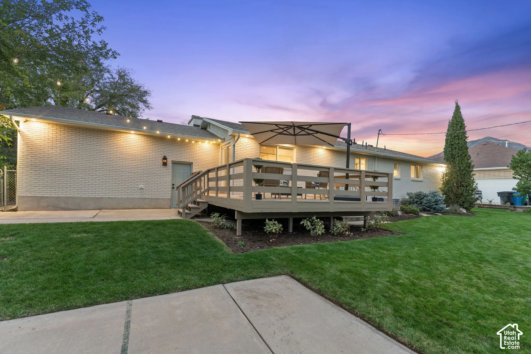 Painted brick exterior featuring a raised wood deck, concrete patio, and landscaped lawn