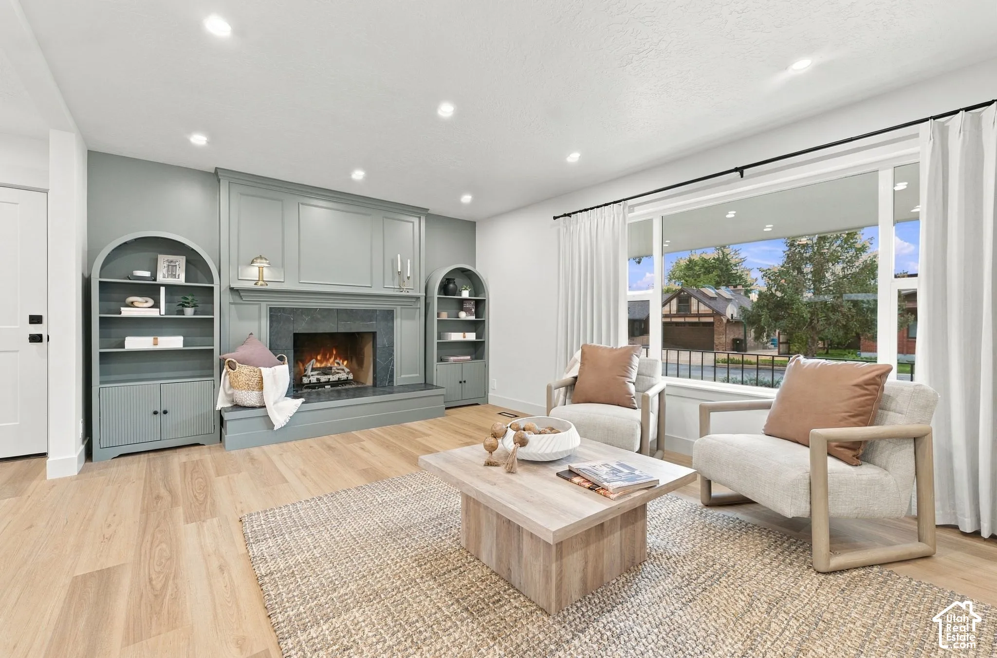 Living area featuring recessed lighting, light-tone wood-finish flooring, and a fireplace with a stone surround