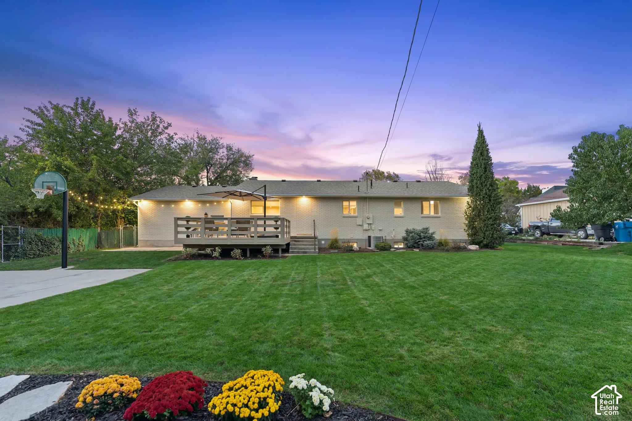 Expansive backyard featuring a manicured lawn, raised wooden deck, concrete sport court, and mature landscaping