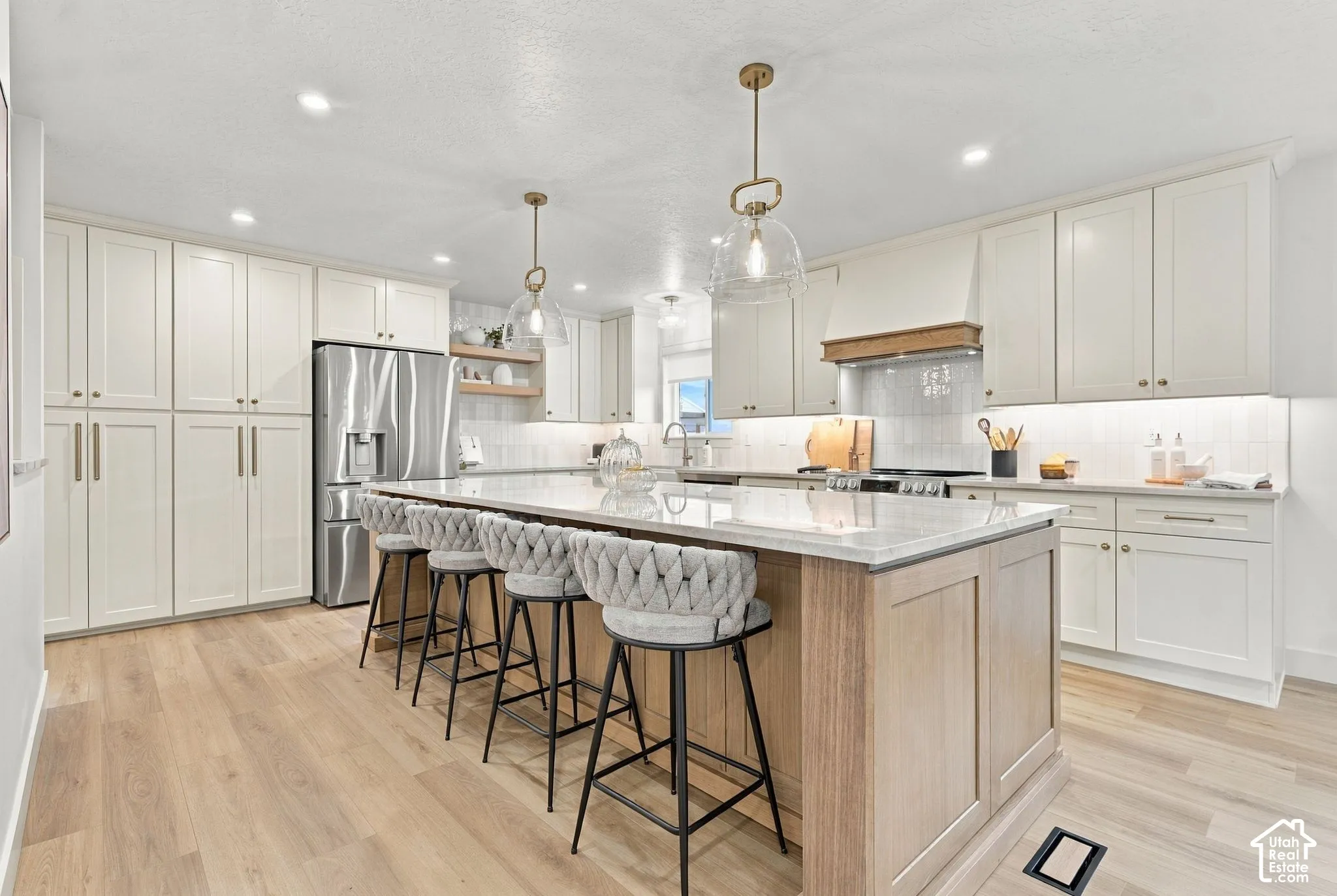 Kitchen featuring custom cabinetry, a central island with stone countertop, stainless steel appliances, wood-finish flooring, and glass pendant lighting