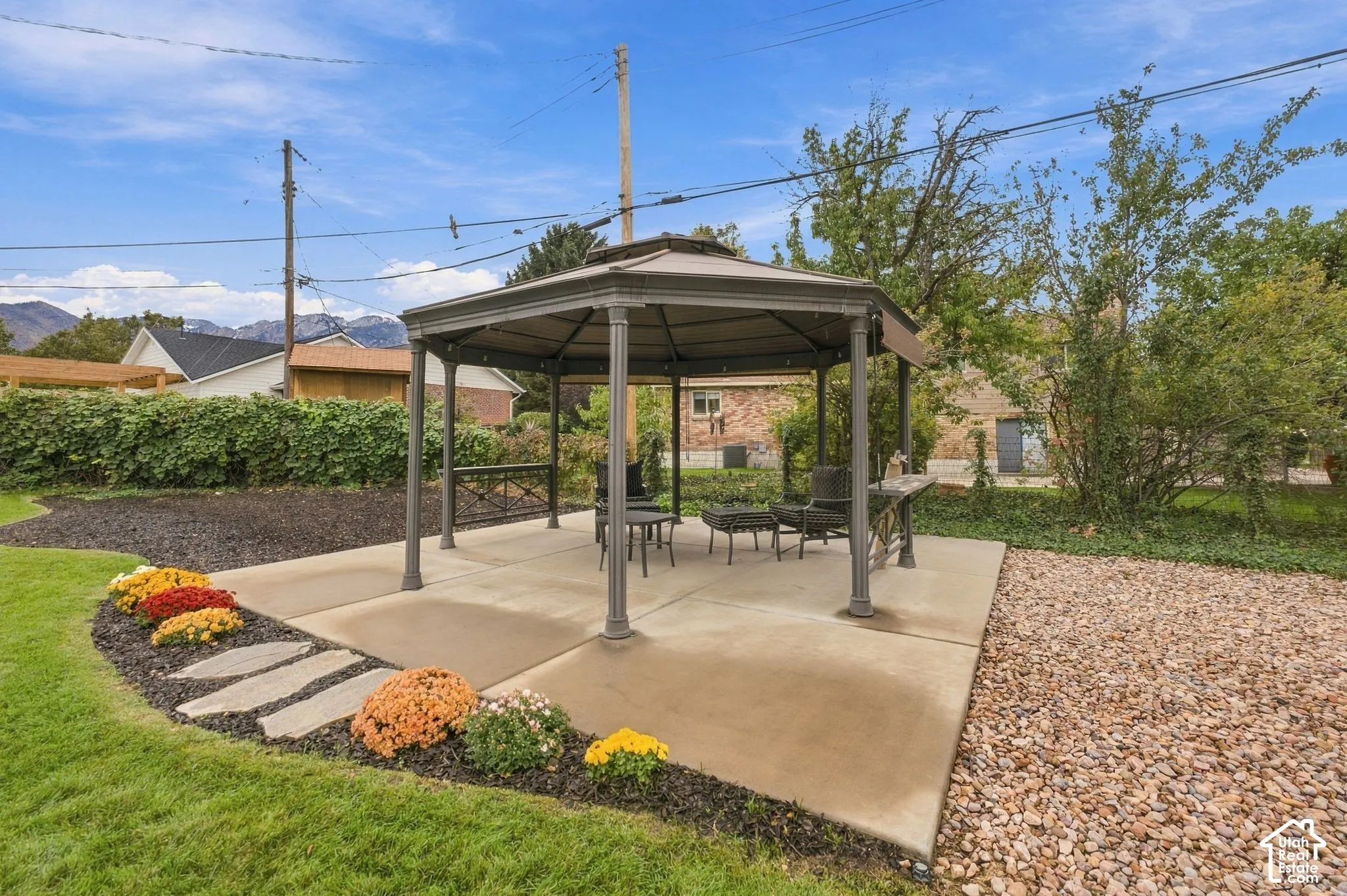 Hexagonal metal-framed pavilion situated on a concrete patio, complemented by natural stone pathways, gravel hardscaping, and mature landscaping