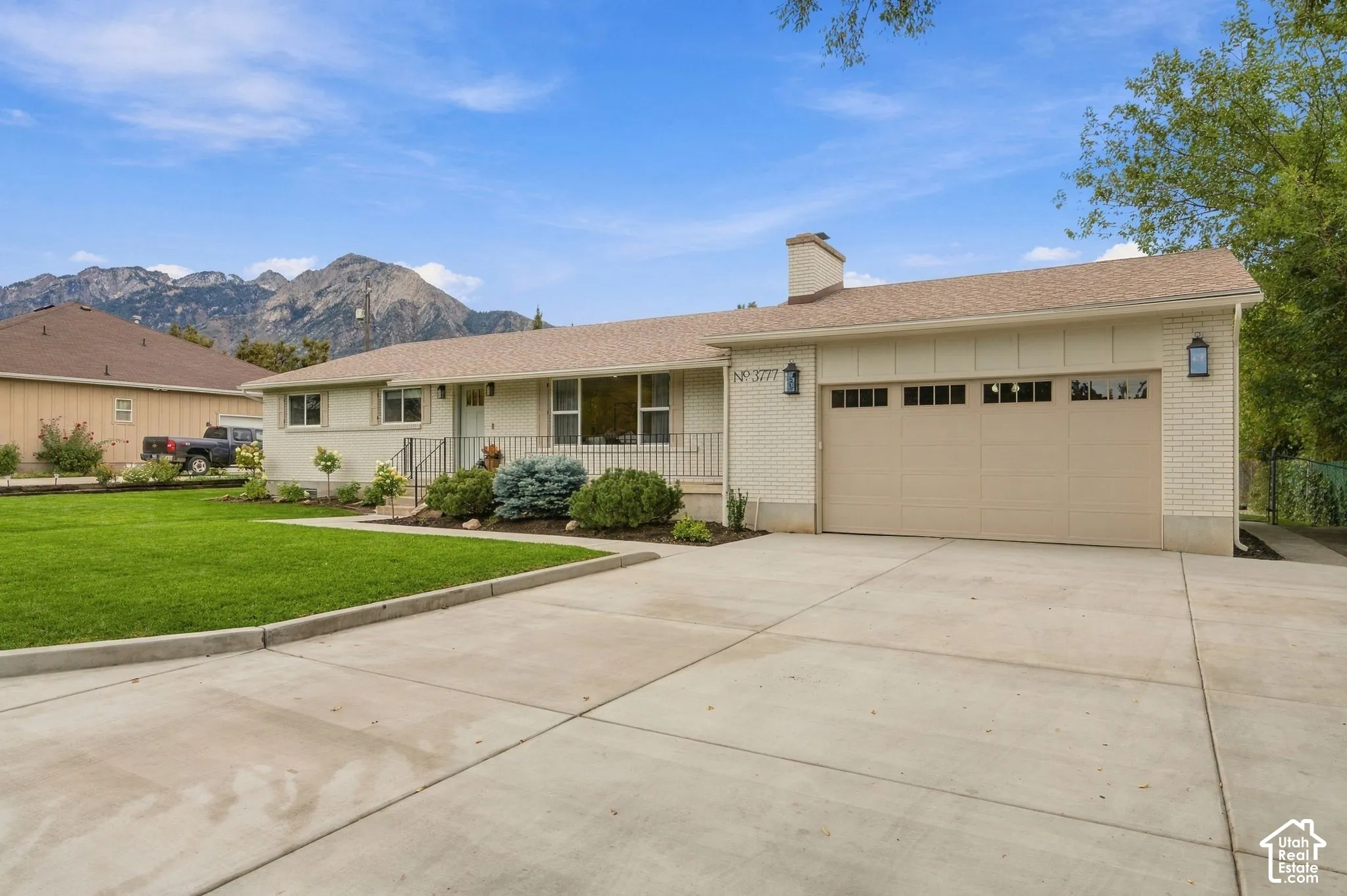 Single-story brick exterior featuring a concrete driveway, two-car garage, mountain backdrop, and manicured landscaping