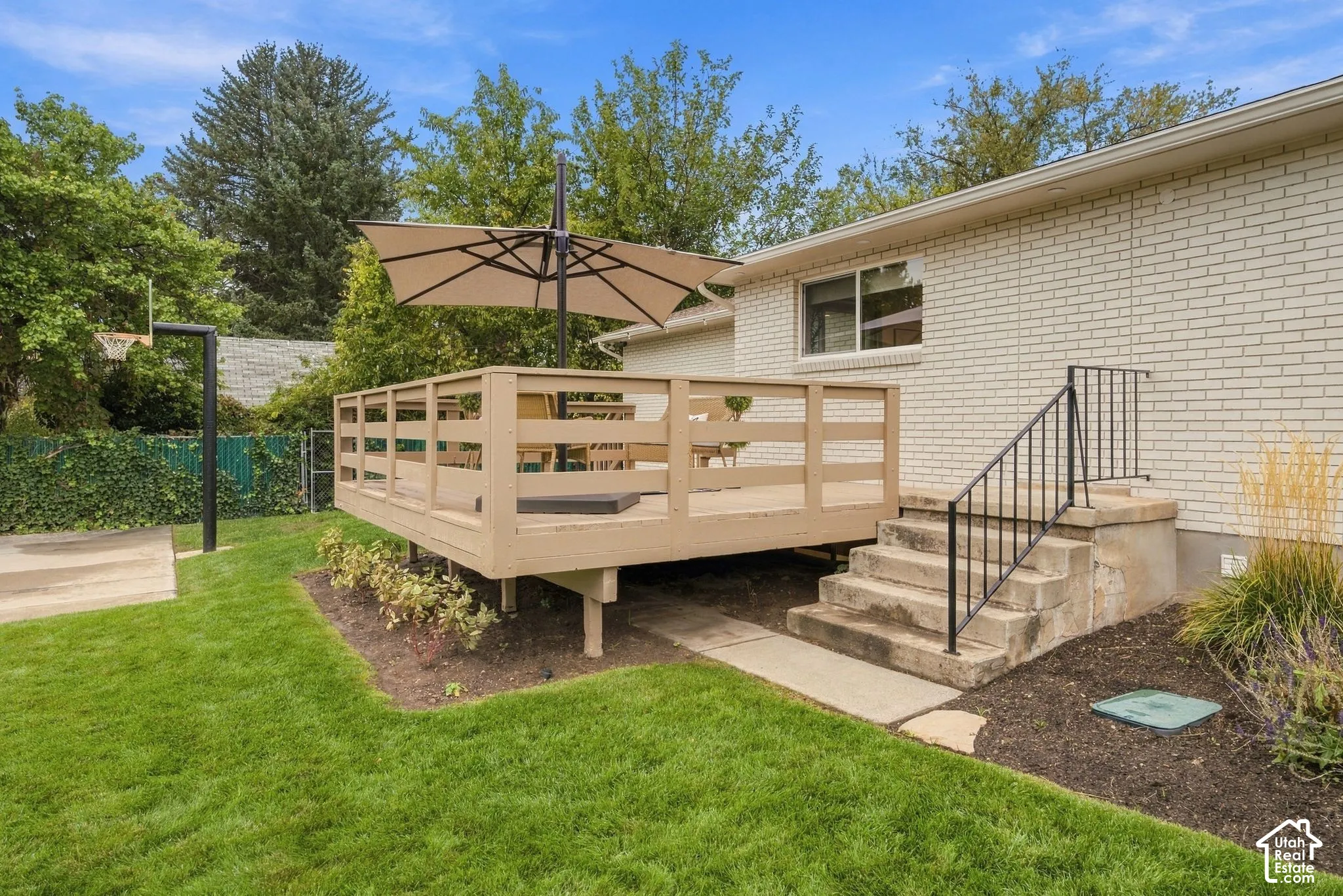 Raised wooden deck with horizontal railing, brick exterior, concrete steps with metal handrail, and landscaped lawn
