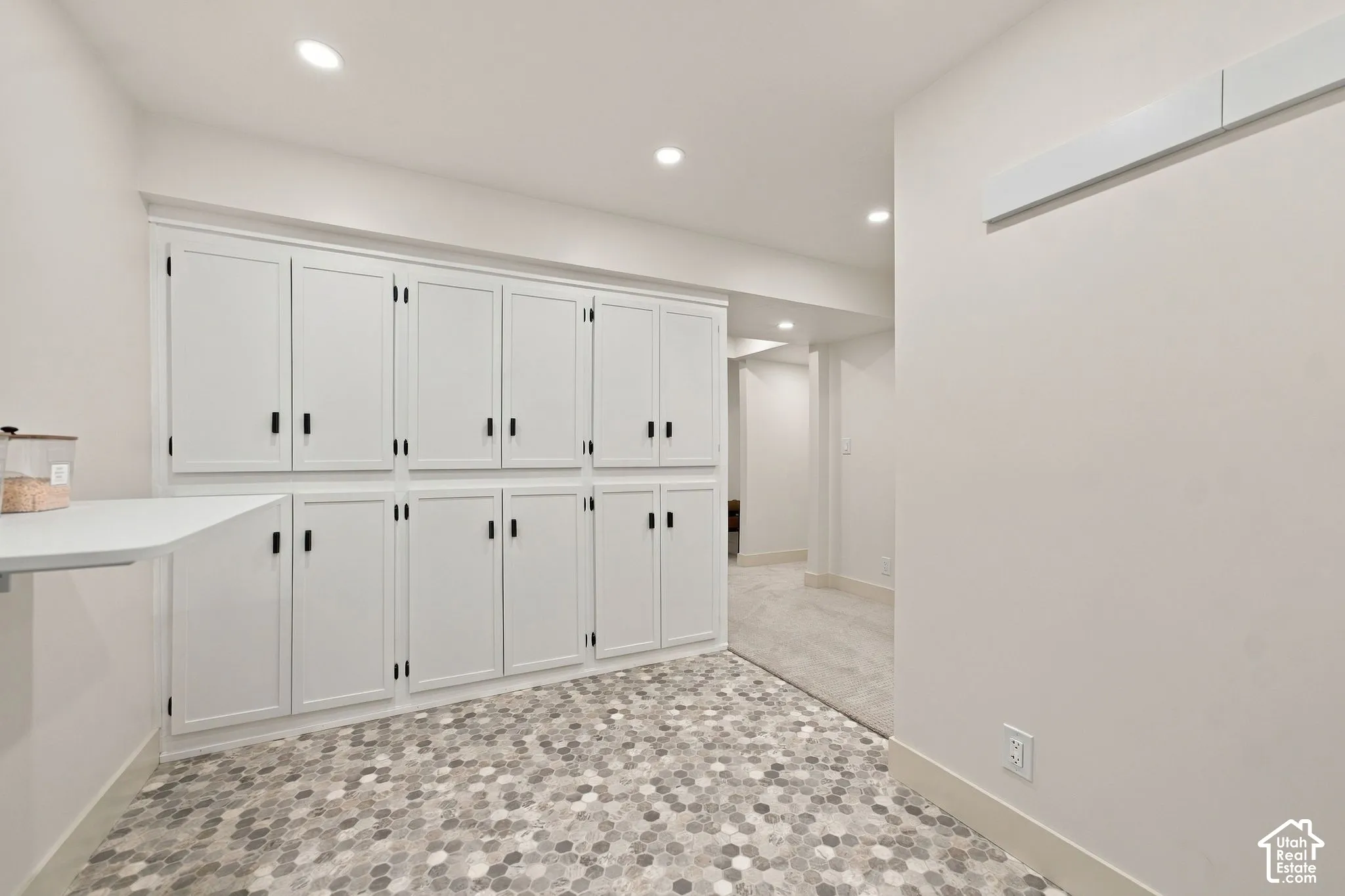 Extensive white built-in cabinetry with matte black hardware, stone-finish hexagonal floor tile, and recessed ceiling lighting