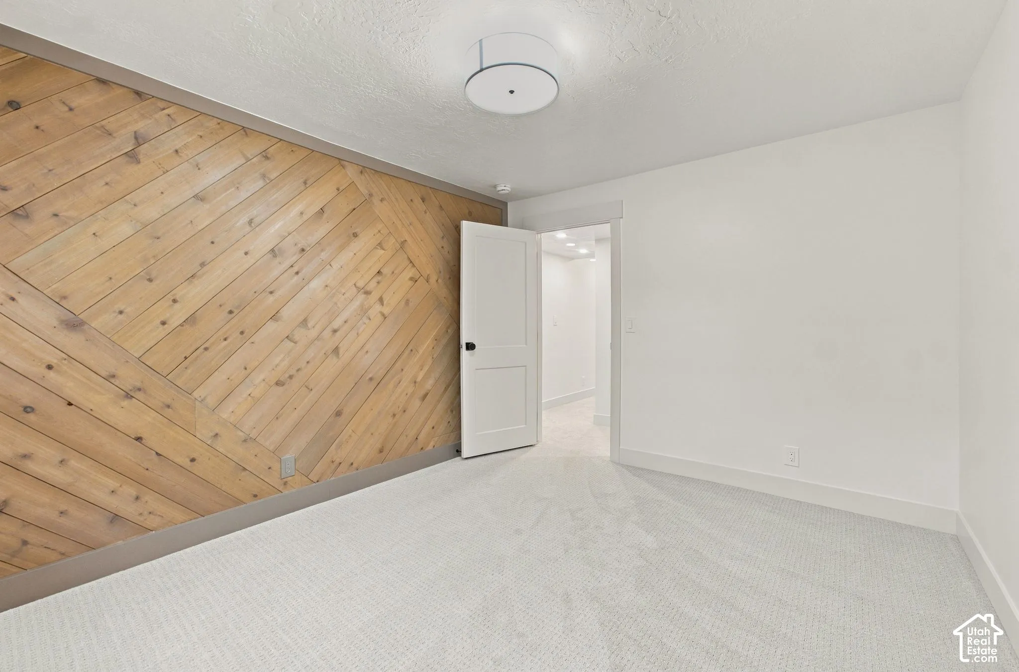 Diagonal wood-plank accent wall, neutral carpeting, and a modern drum-style ceiling light fixture