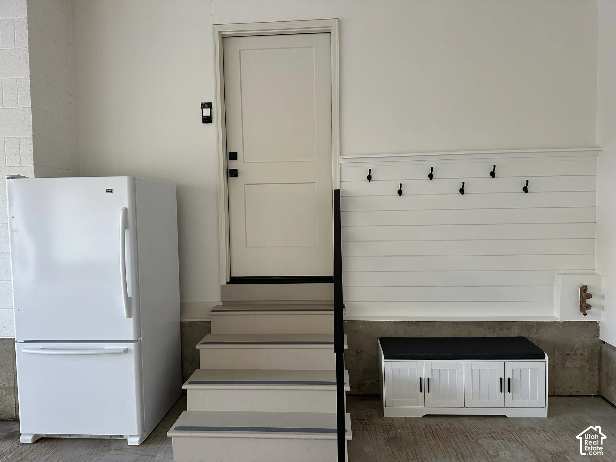 Shiplap wall paneling with integrated coat hooks, built-in cabinetry, and a set of stairs with a metal handrail
