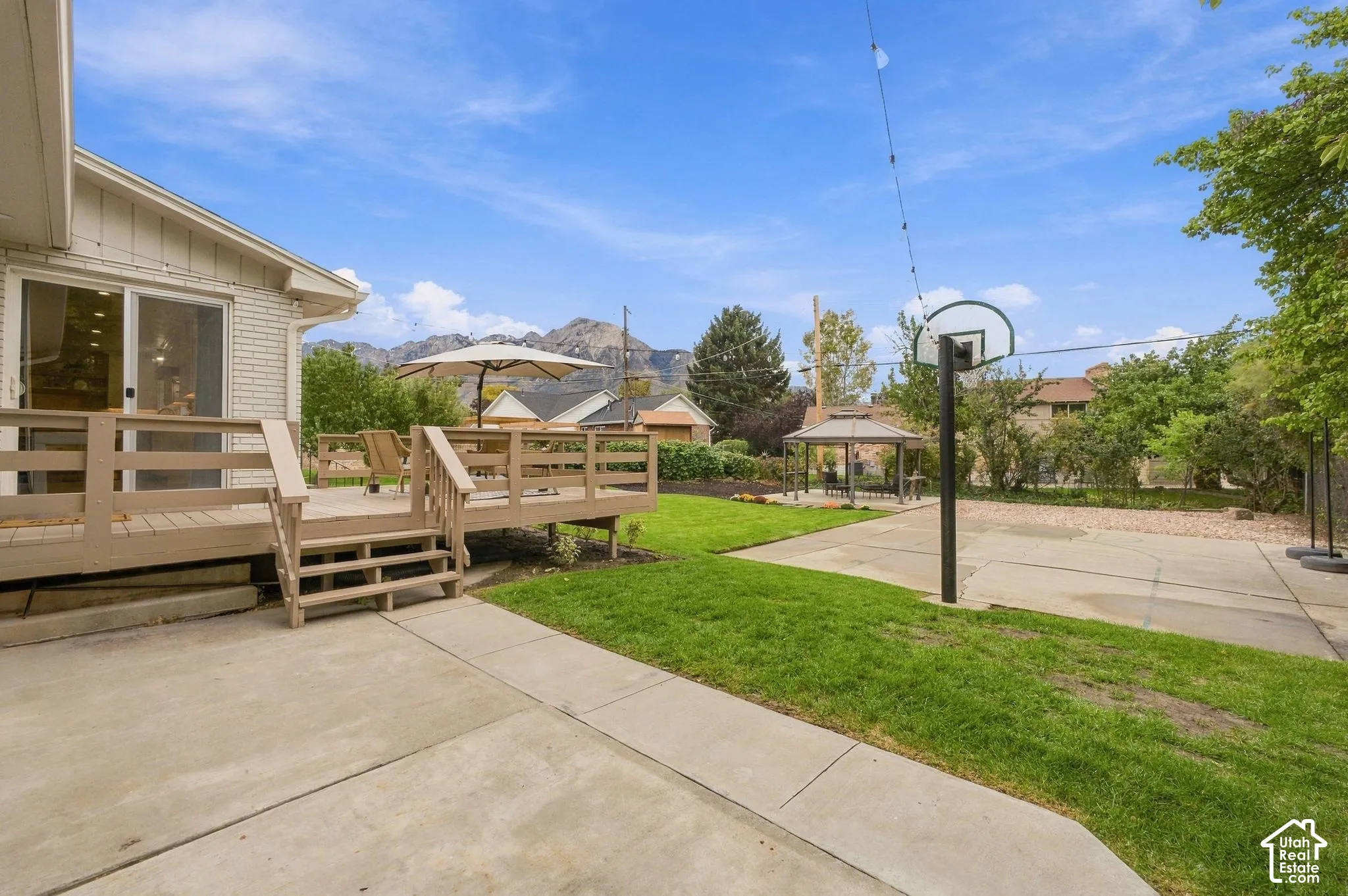 Rear exterior featuring a raised wood deck, concrete patio, dedicated sport court area, and mountain backdrop
