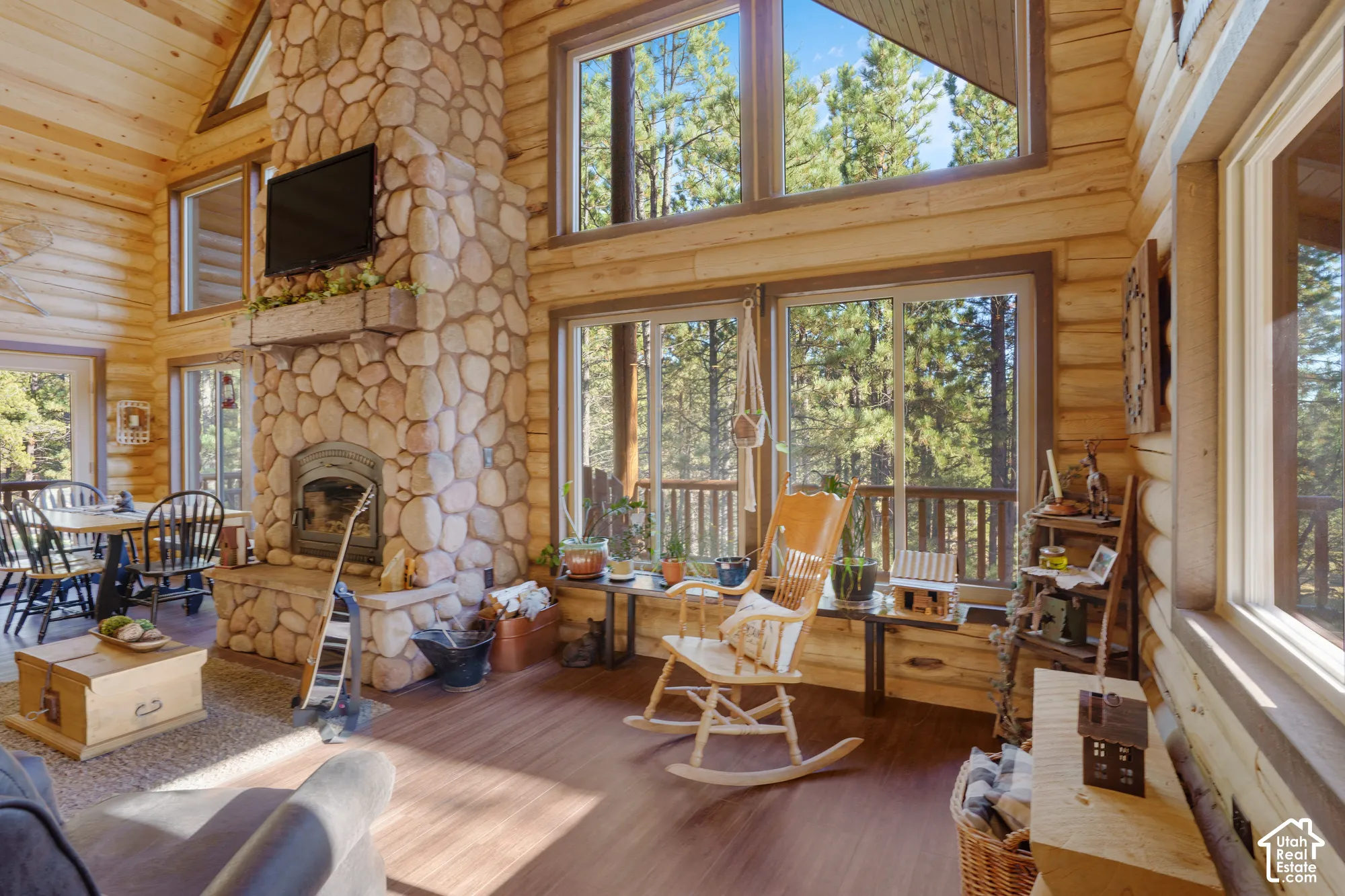 Log wall construction featuring vaulted ceilings, floor-to-ceiling stone fireplace with a timber mantel, and expansive multi-pane windows