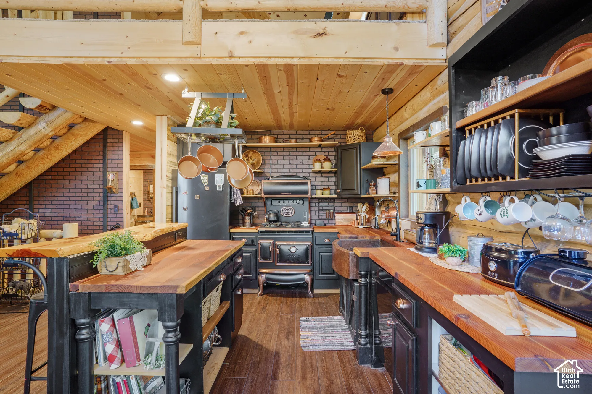 Kitchen featuring live-edge wood countertops, dark cabinetry, brick backsplash, apron-front copper sink, and vintage-style gas range