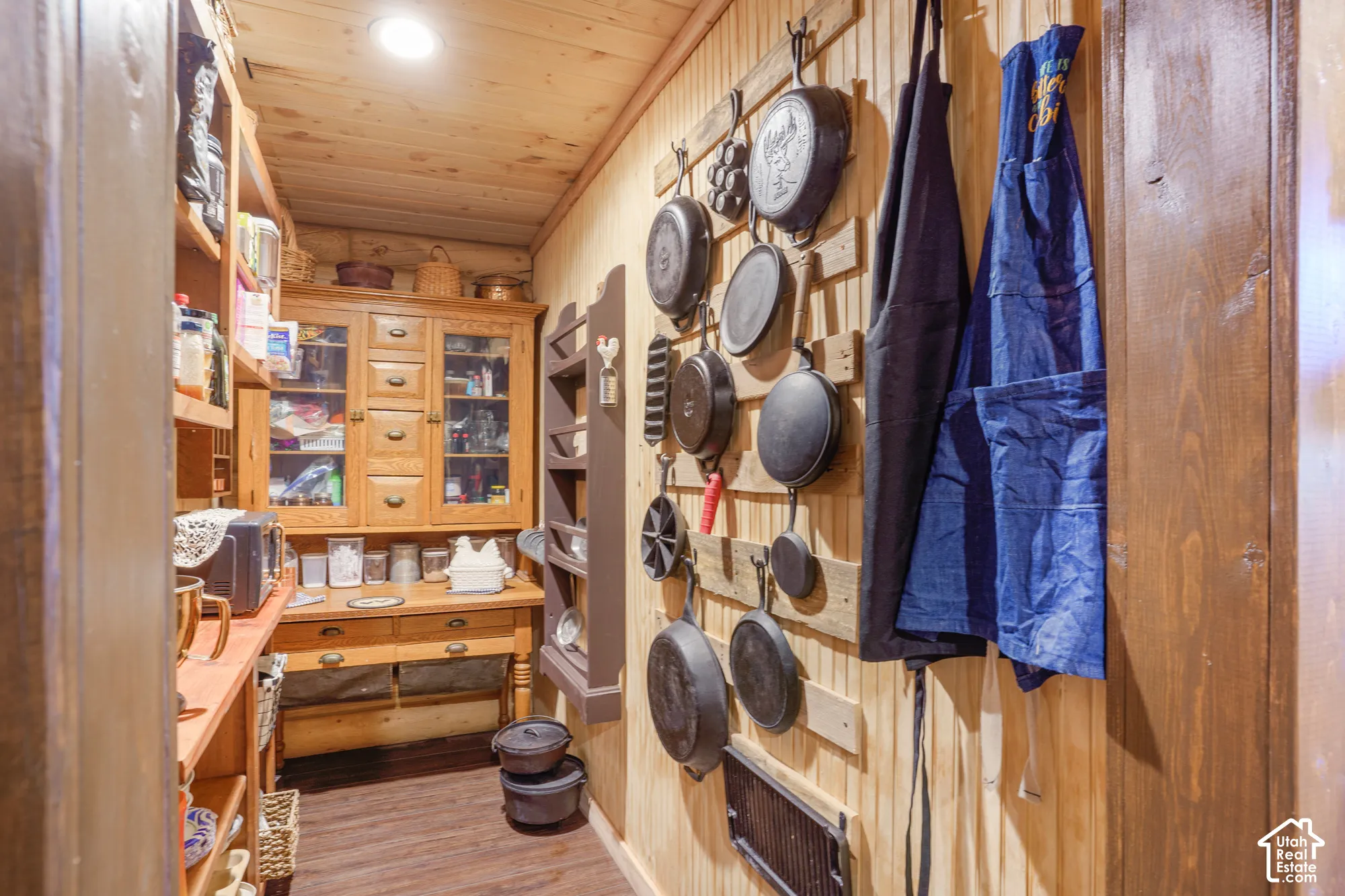 Storage area featuring tongue-and-groove wood wall paneling, built-in floor-to-ceiling shelving, solid wood cabinetry with integrated drawers, and a mounted wood slat wall rack
