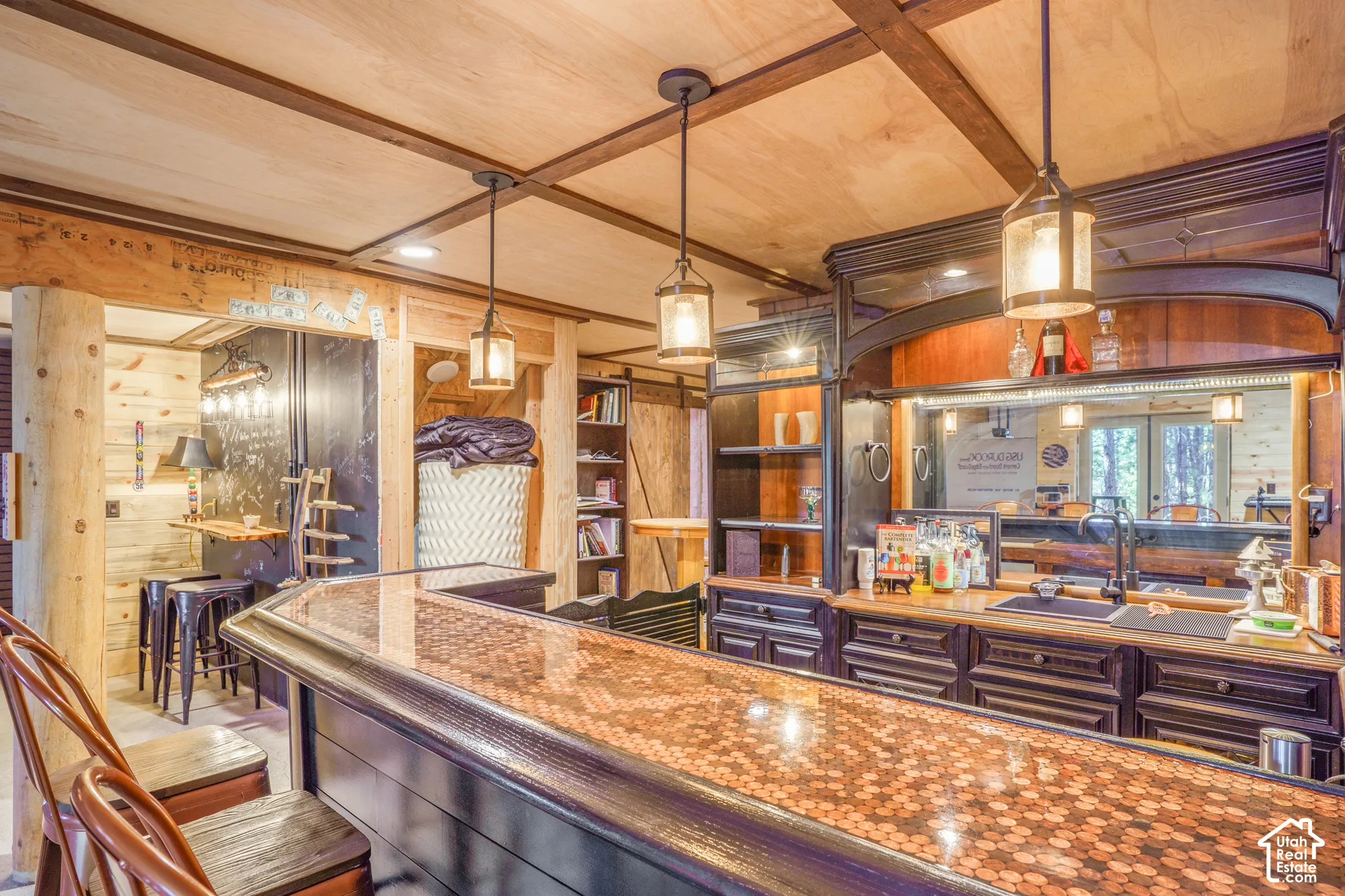 Custom wet bar featuring a copper-top peninsula, dark wood cabinetry, integrated mirrored backsplash, panelled ceiling with exposed beams, and decorative pendant lighting
