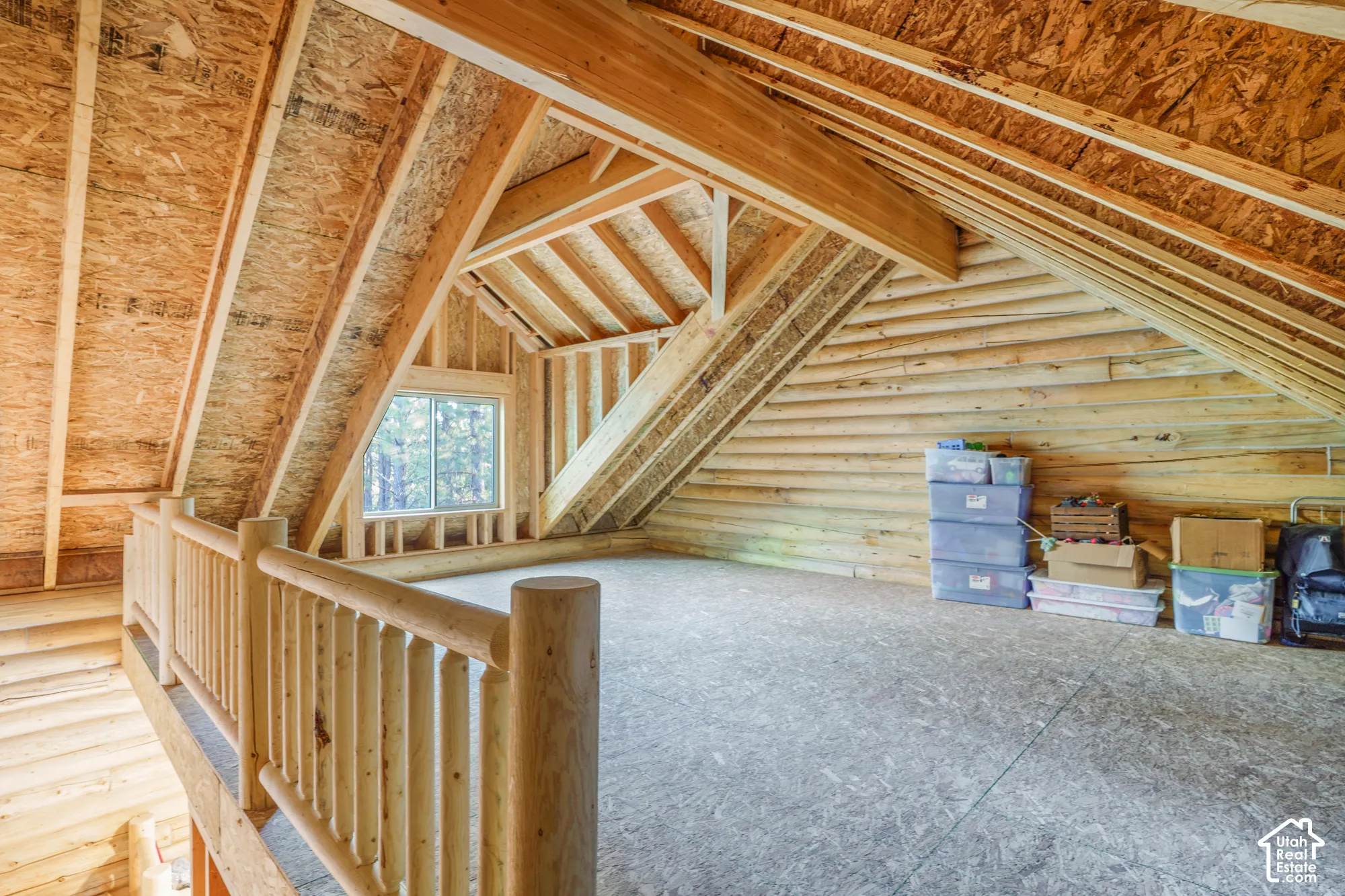 Open-concept loft area featuring exposed log walls, timber framing, vaulted ceilings with oriented strand board sheathing, and a custom log railing