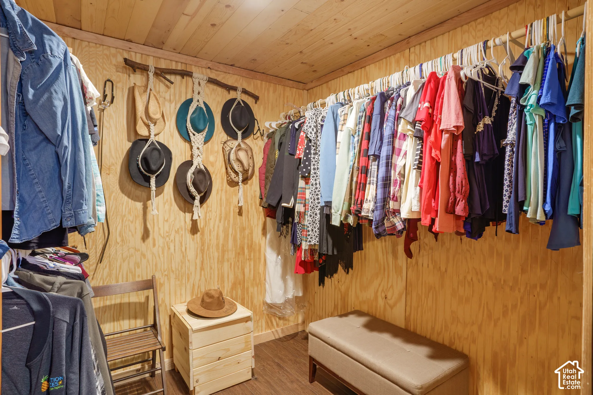 Walk-in closet featuring plywood wall paneling, natural wood-plank ceiling, and wood-finish flooring with dual-level hanging storage rods