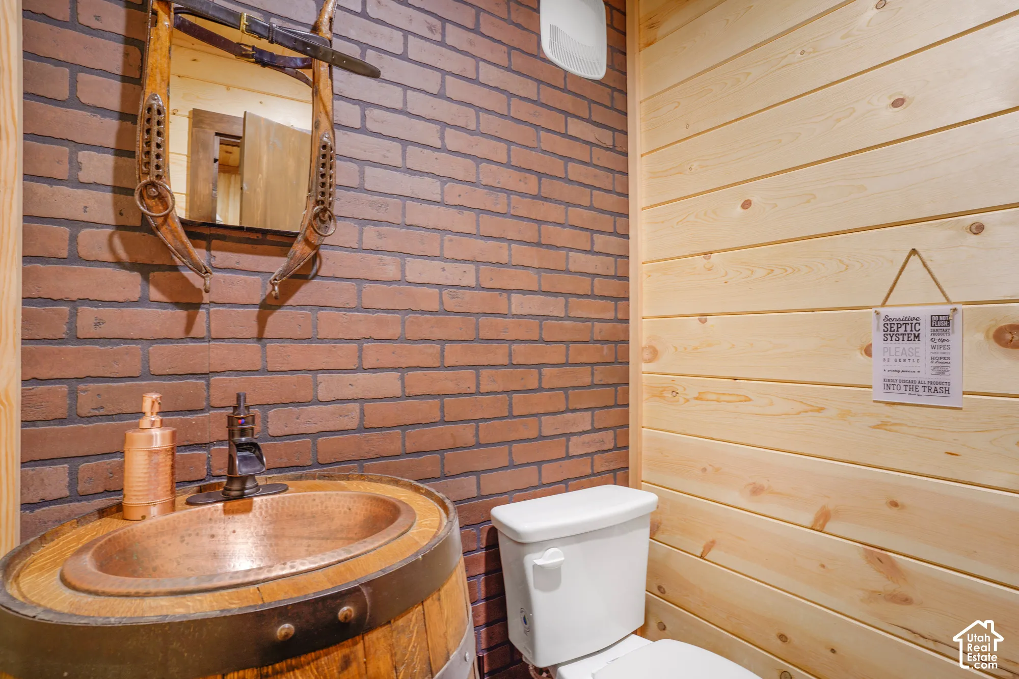 Exposed brick wall paired with horizontal wood paneling, featuring a custom barrel vanity, integrated copper sink basin, and metallic faucet fixture