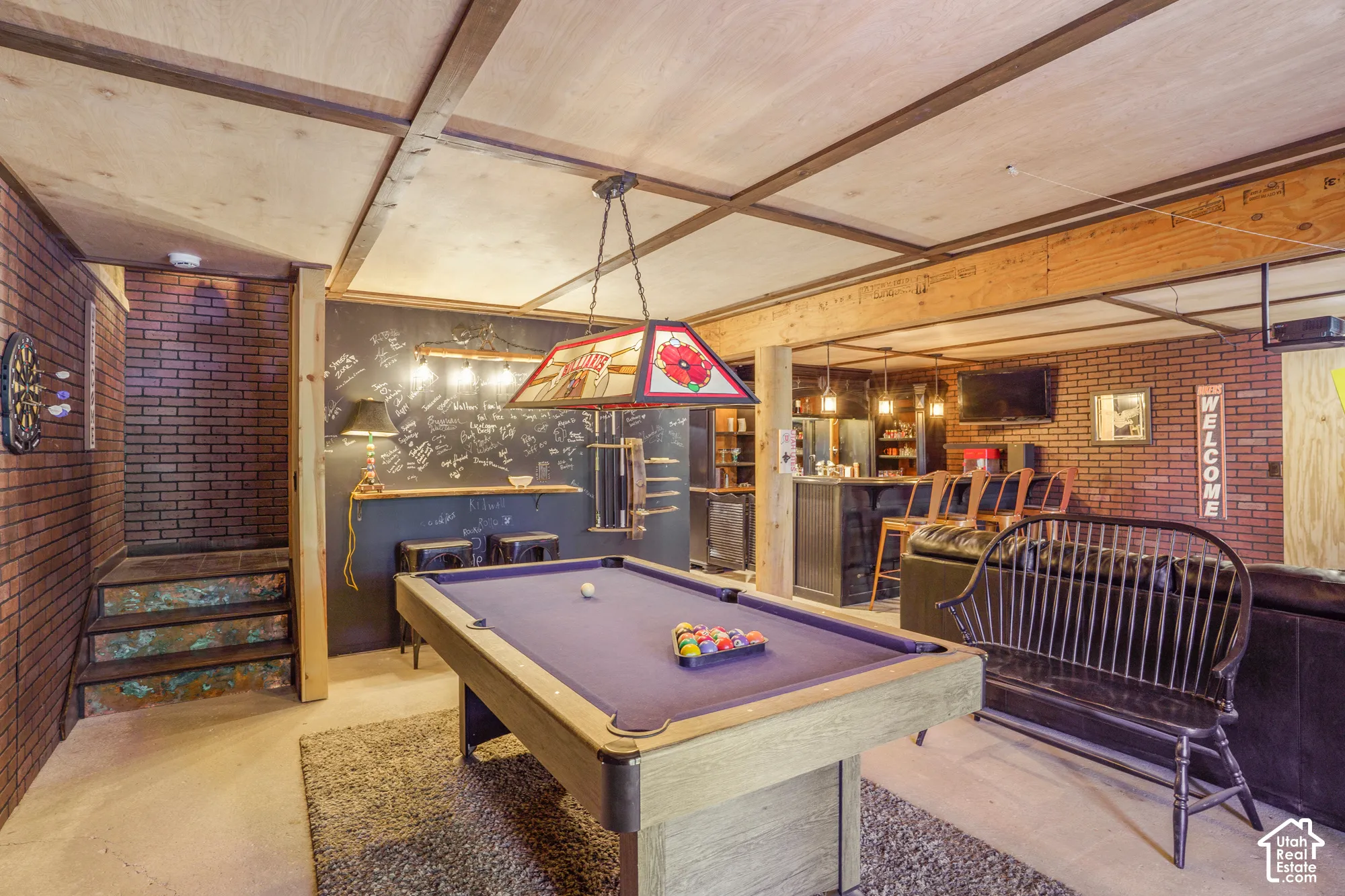 Finished interior space featuring exposed brick walls, custom wood-paneled ceiling with support beams, built-in bar with dark cabinetry, and concrete flooring