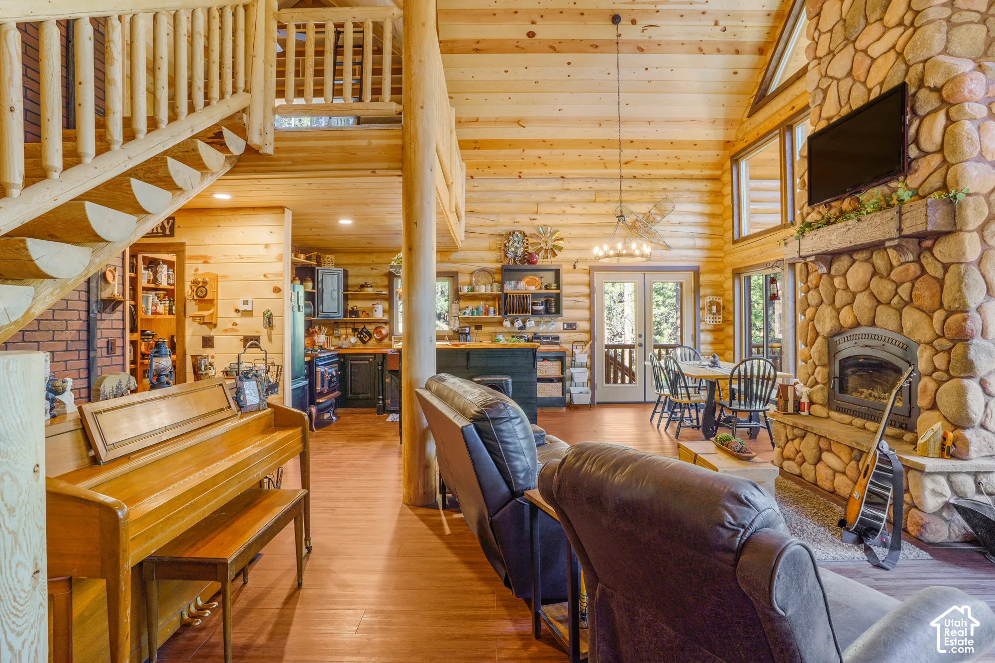 Log-construction interior featuring a floor-to-ceiling river stone fireplace, vaulted tongue-and-groove wood ceilings, a prominent log staircase, and wood-finish flooring