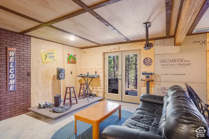 Interior space featuring exposed wood-plank walls, paneled ceiling with dark timber beams, a red brick accent wall, and double glass-paned doors