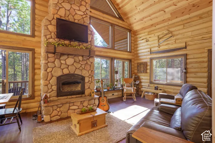Vaulted ceilings with exposed timber beams, floor-to-ceiling stone fireplace, stacked log walls, and expansive windows