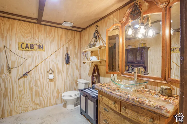 Wood-paneled wall finish, vanity with embedded stone countertop, glass vessel sink, and custom rope-suspended lighting fixture