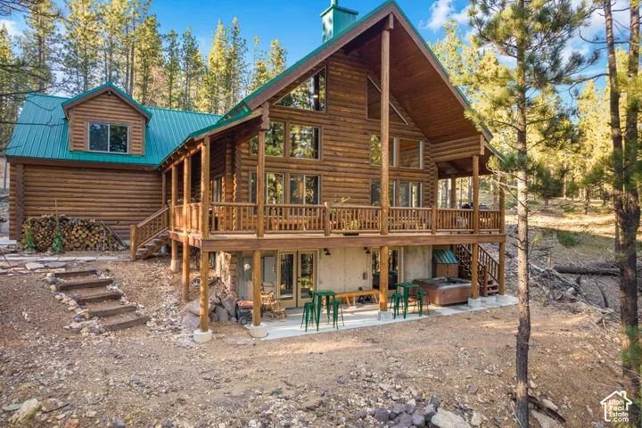 Log cabin exterior featuring a multi-level wood deck, green standing-seam metal roofing, large multi-pane windows, and a covered lower-level concrete patio