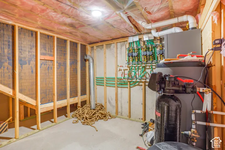 Utility space featuring concrete flooring, framed wall partitions, a multi-zone water manifold system, and a tank-style water heater