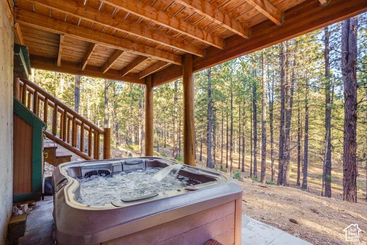 Covered outdoor patio featuring a built-in hot tub, exposed beam ceiling, timber structural posts, and natural forest landscape