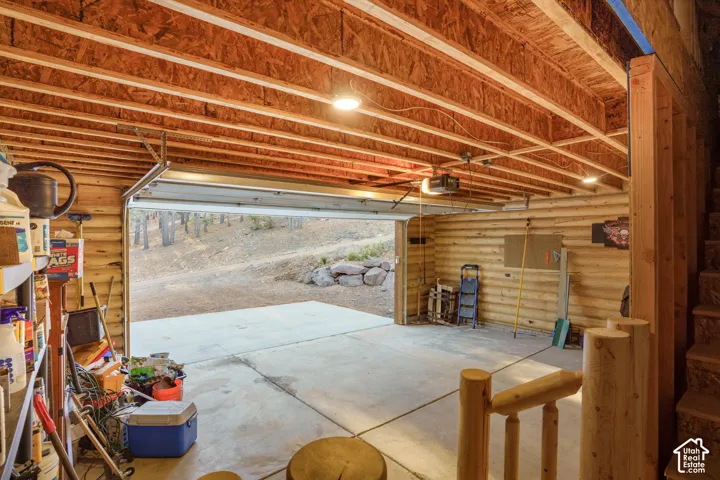 Garage featuring exposed ceiling joists, log walls, concrete flooring, and an automatic door opener