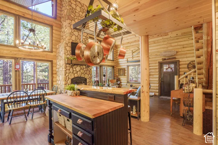 Log construction interior featuring a stone-clad hearth, wood-finish flooring, a kitchen island with a wood countertop, and floor-to-ceiling windows