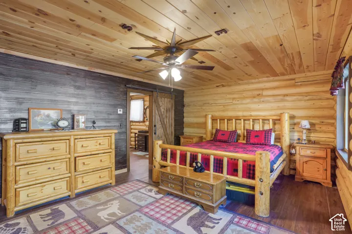 Interior featuring horizontal log walls, reclaimed-style wood-plank accent wall, wood-finish ceiling, wood-plank flooring, and a sliding barn-style door