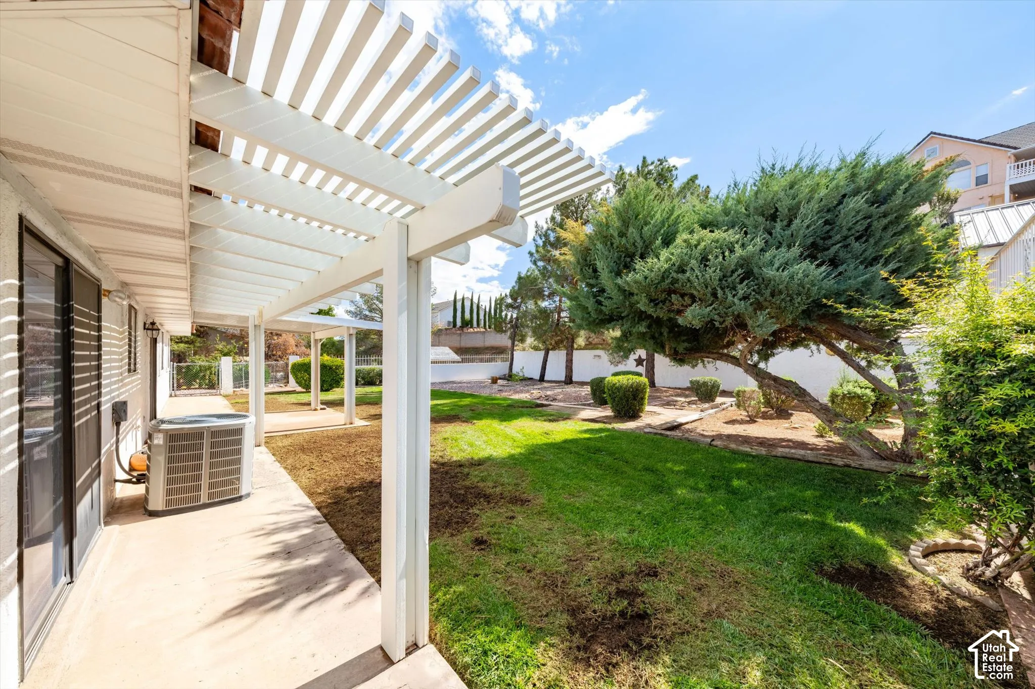 Backyard featuring a white slatted patio cover, concrete patio, grass lawn, mature specimen trees, and perimeter masonry wall