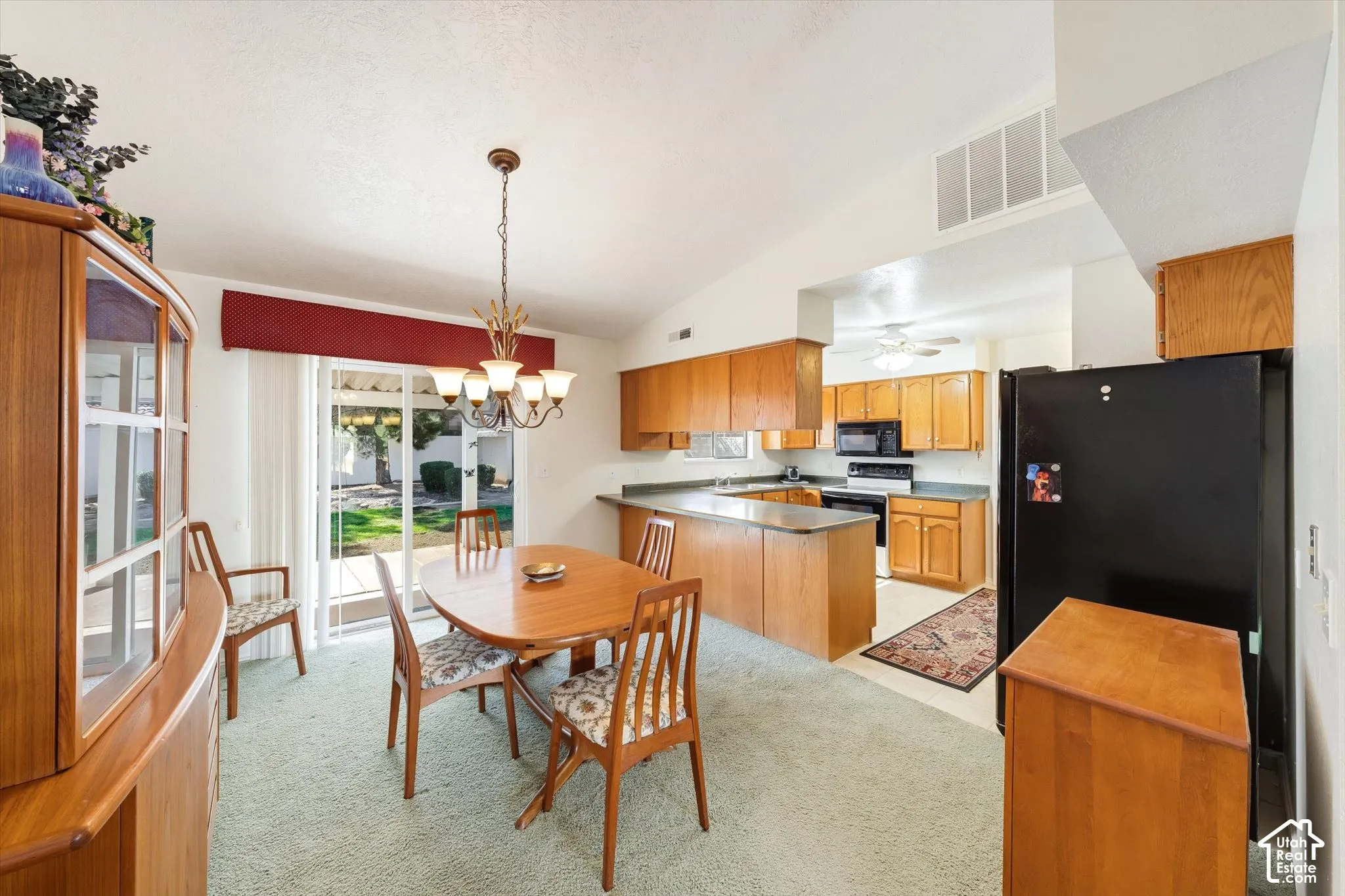 Kitchen featuring wood cabinetry, a breakfast bar, and integrated black appliances, paired with a dining area illuminated by a multi-light chandelier and sliding glass doors