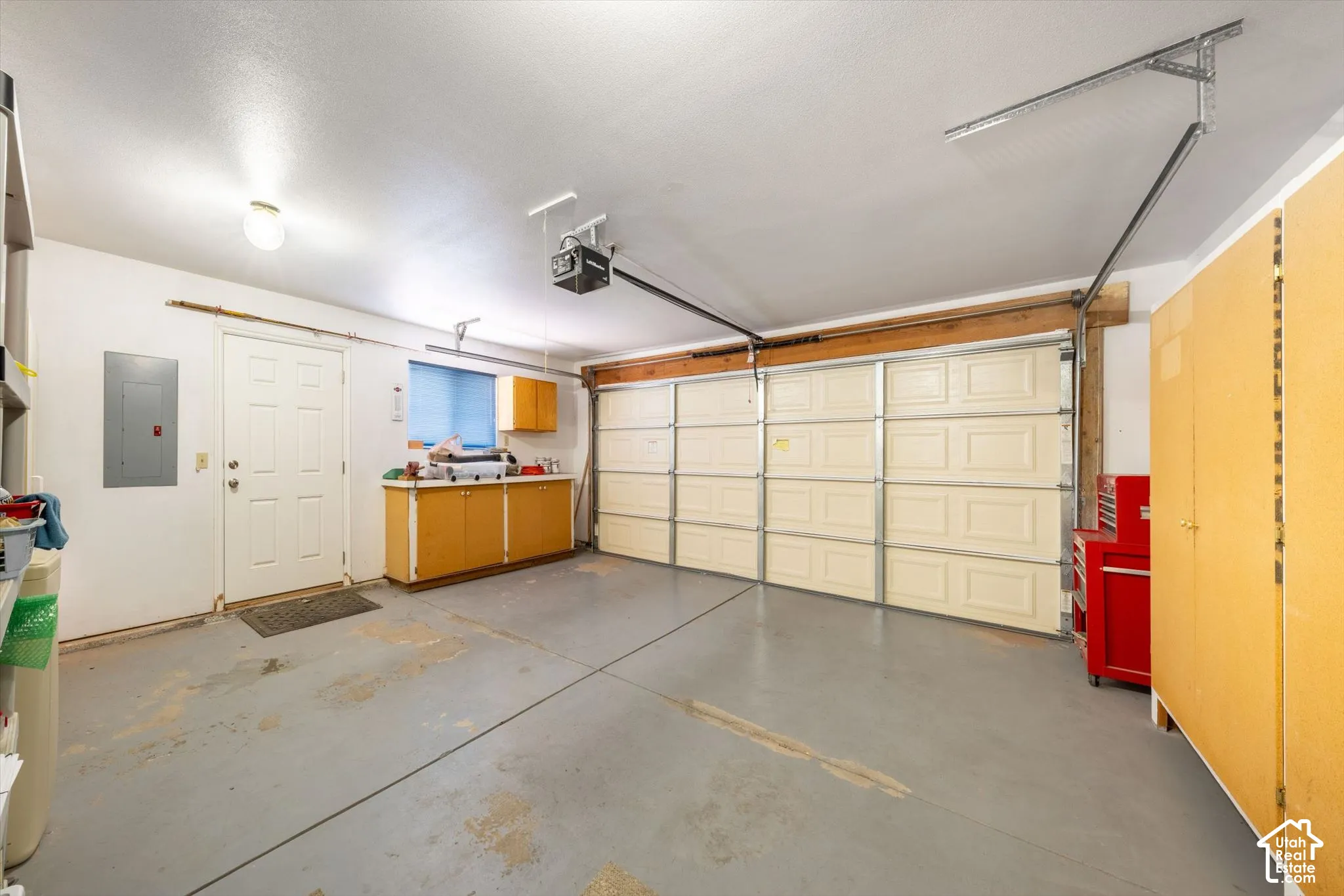 Multi-car garage featuring a sectional overhead door, painted concrete flooring, built-in lower cabinetry with laminate countertops, integrated overhead lighting, and dedicated wall-mounted storage units