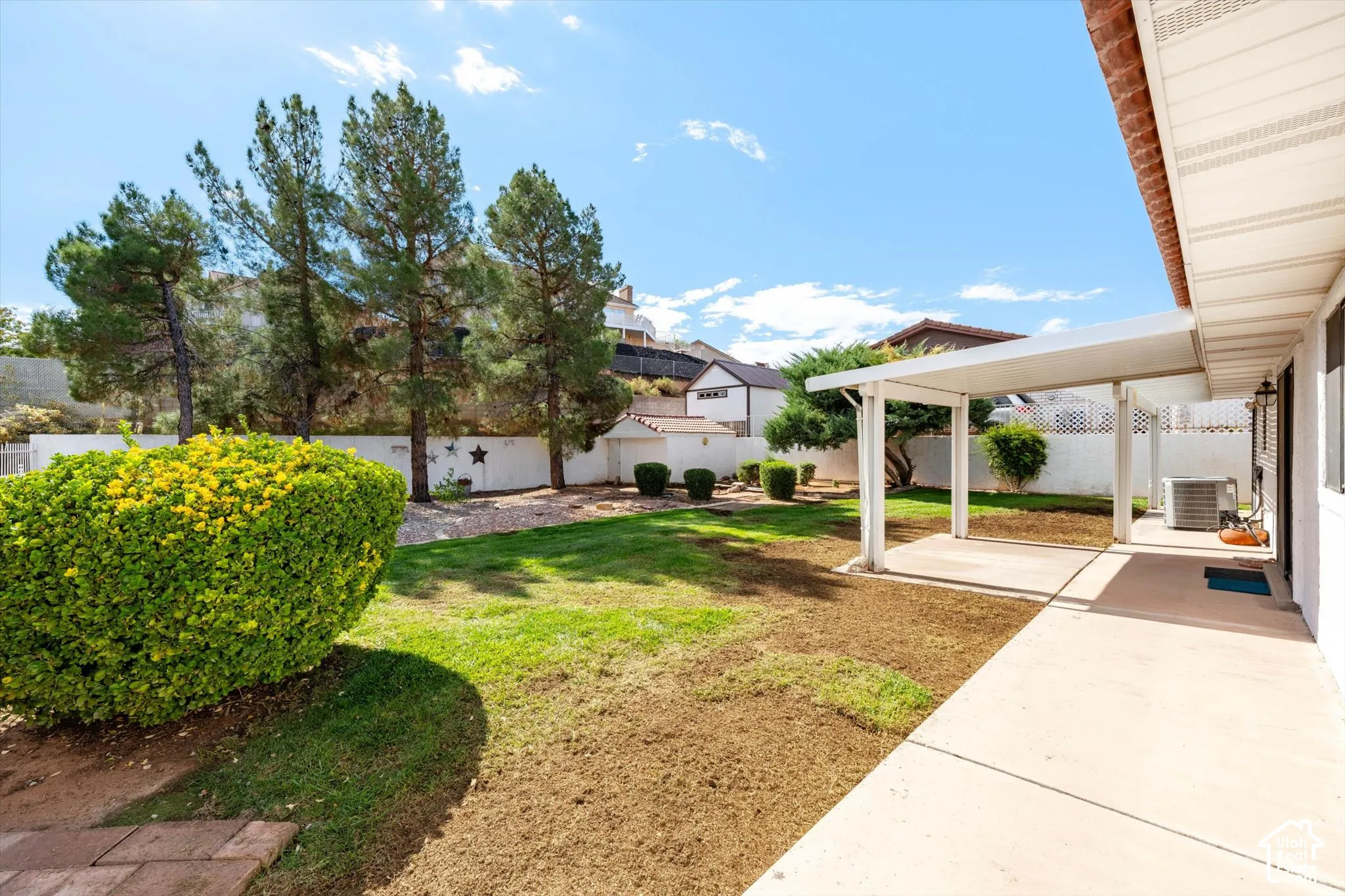Backyard featuring a covered patio, lawn area, perimeter masonry wall, mature trees, and a detached structure