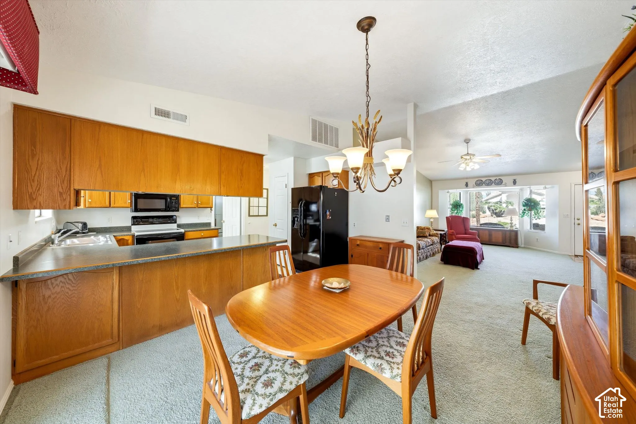 Kitchen featuring wood cabinetry, a breakfast bar, and integrated black appliances, complemented by a multi-arm metal chandelier and carpeted flooring