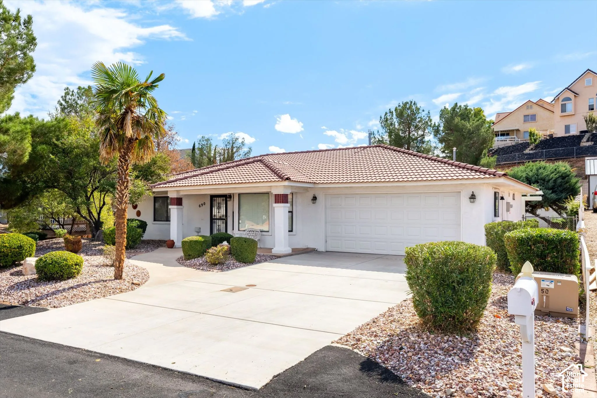 Single-story residence featuring a tile roof, covered front entryway with structural columns, concrete driveway, and xeriscaped front yard